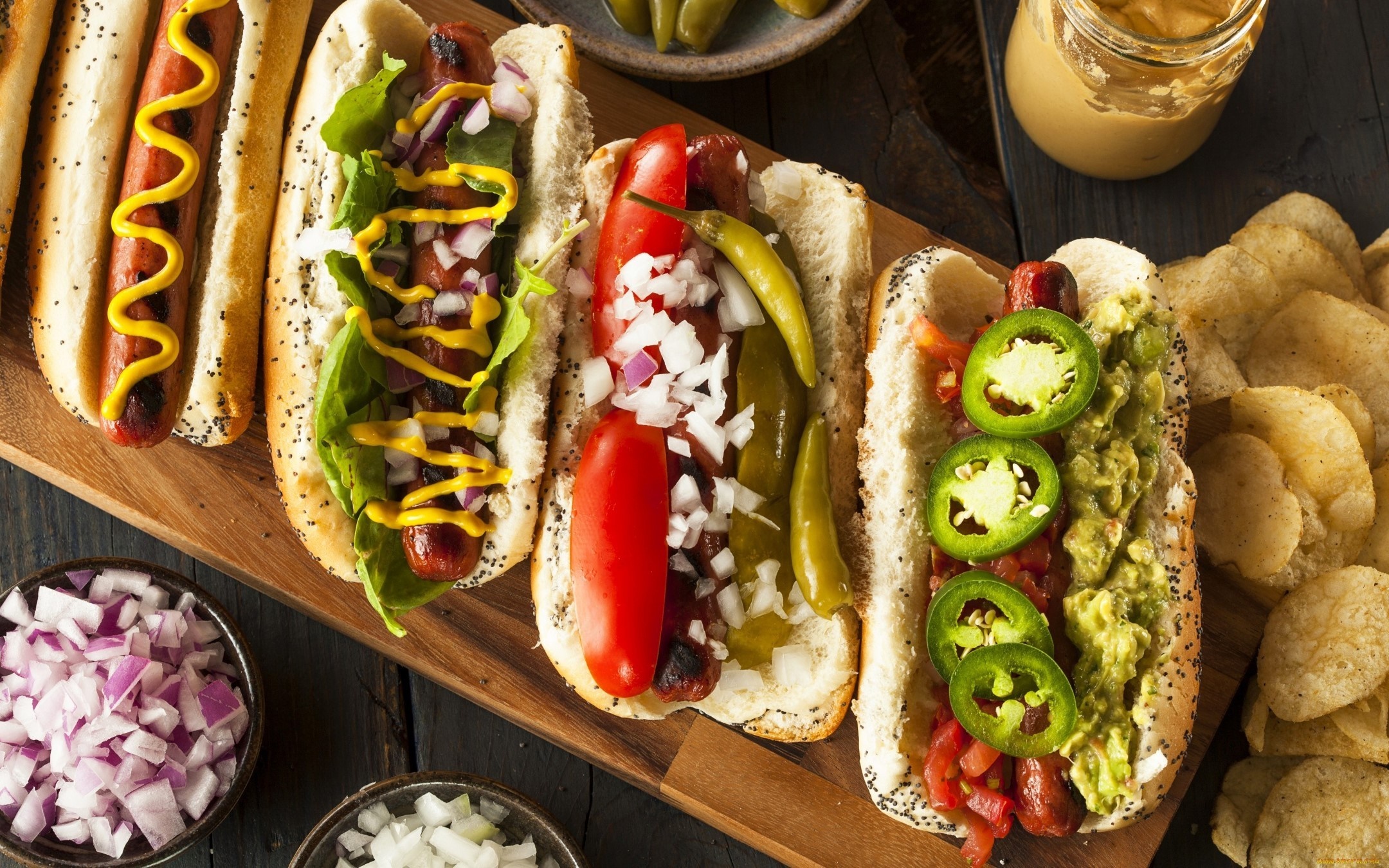 Four gourmet hot dogs with various toppings and sides HD Wallpaper