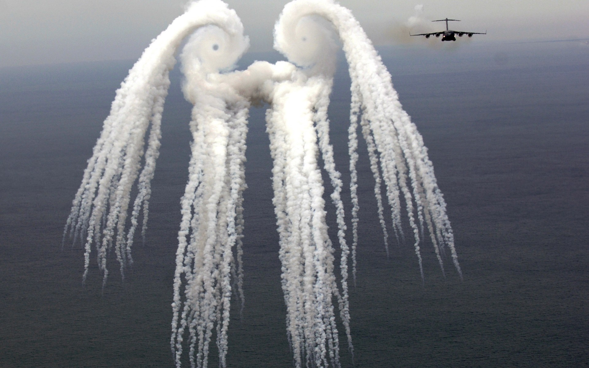 Aircraft releasing smoke trails over the sea HD Wallpaper
