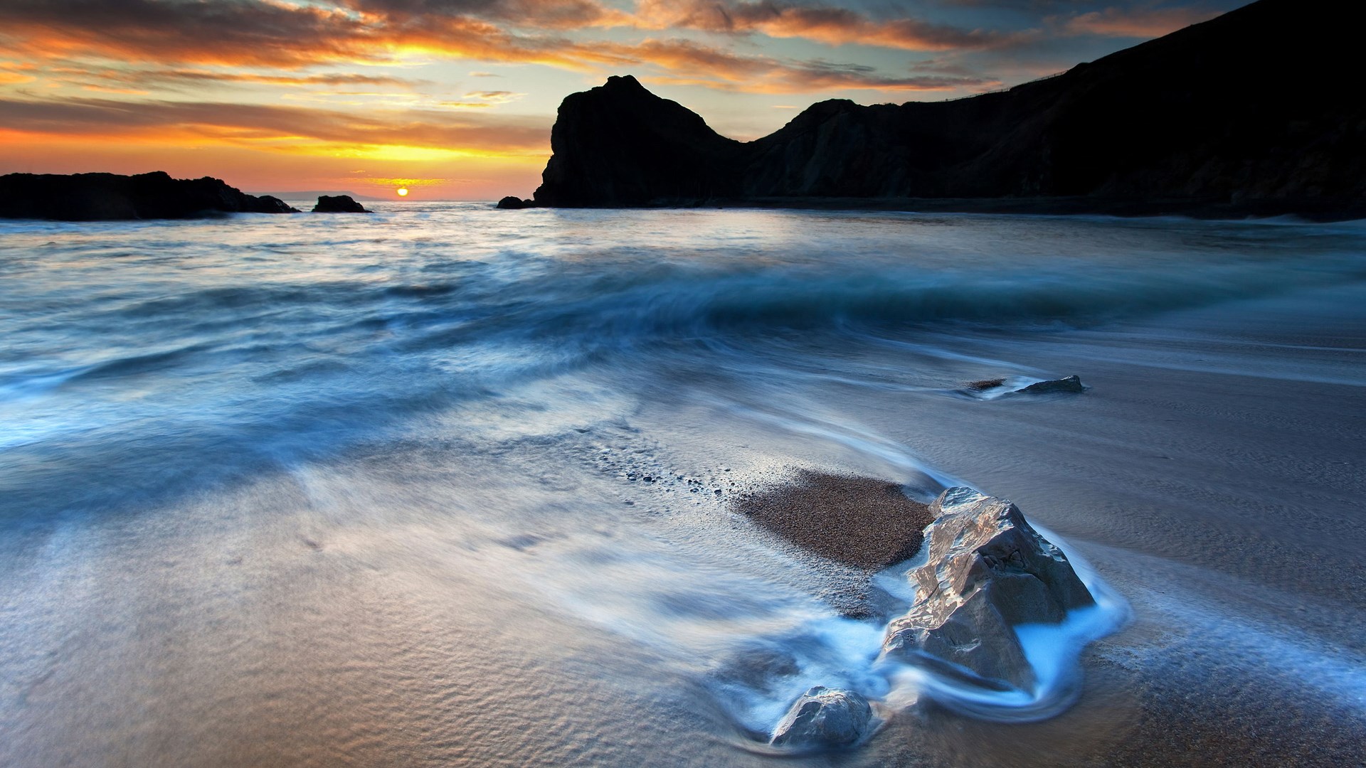 Sunset over a rocky beach with waves HD Wallpaper