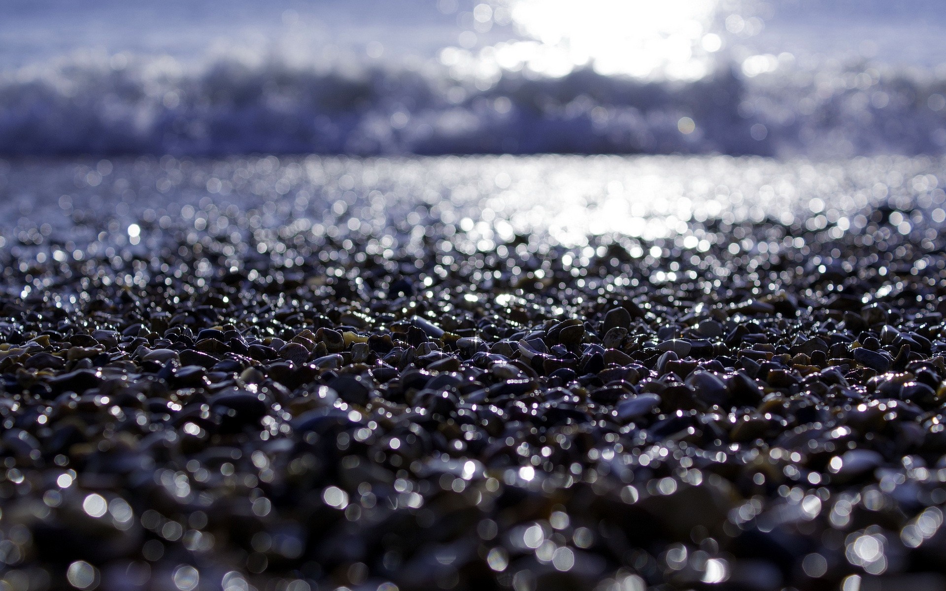 Pebble beach with sunlight reflecting on wet stones and waves HD Wallpaper