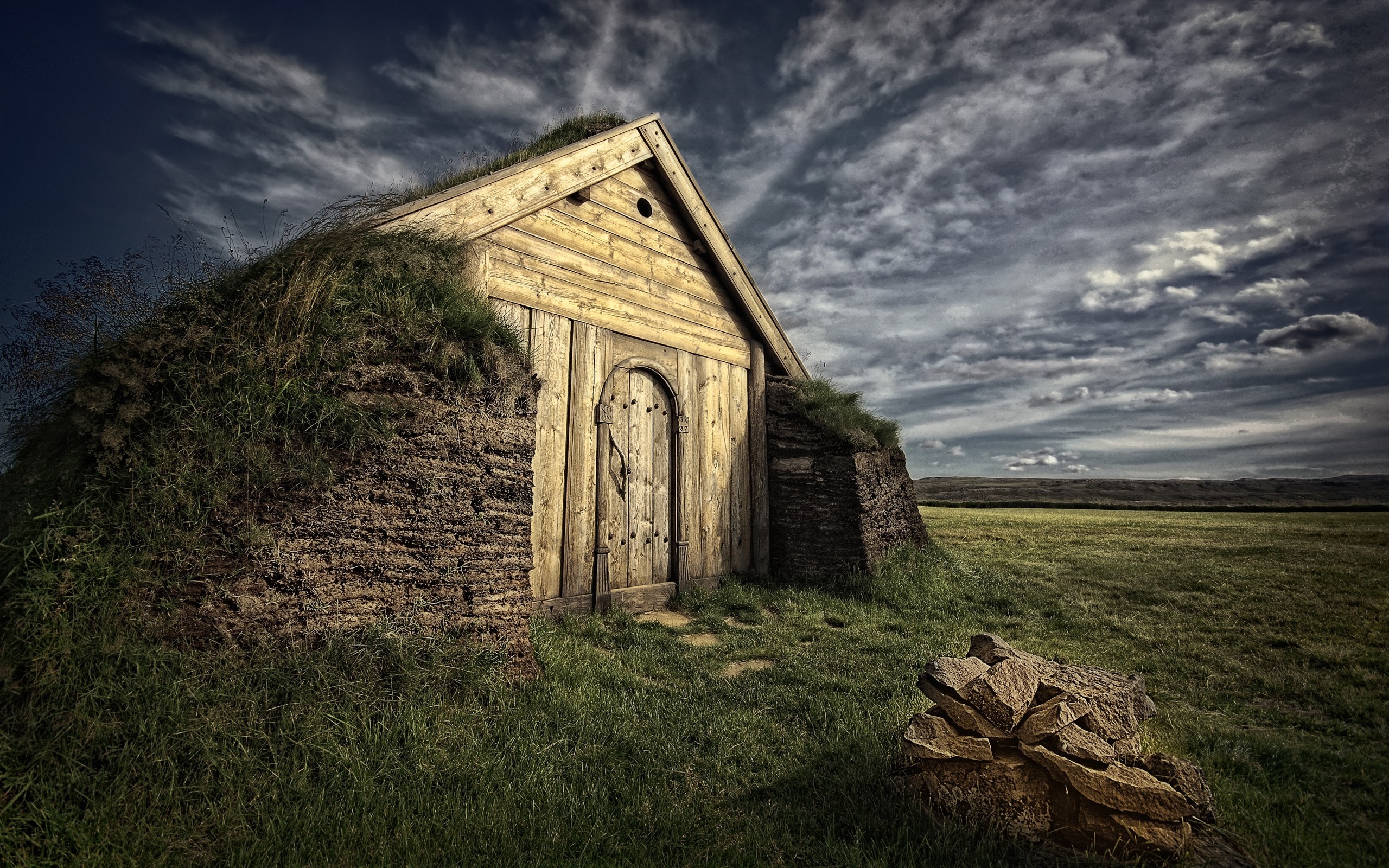 Grass-covered building with wooden door in a field HD Wallpaper