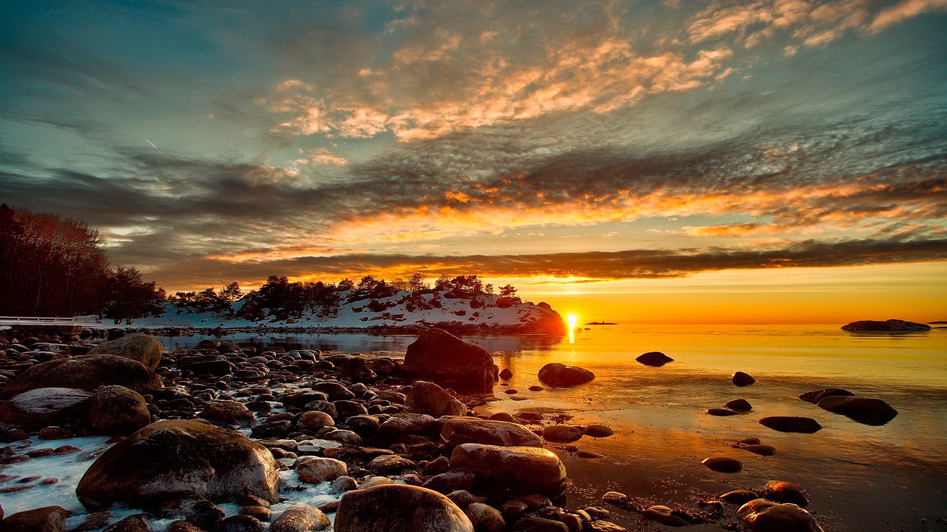 Sunset over a rocky shore with snow-covered trees HD Wallpaper