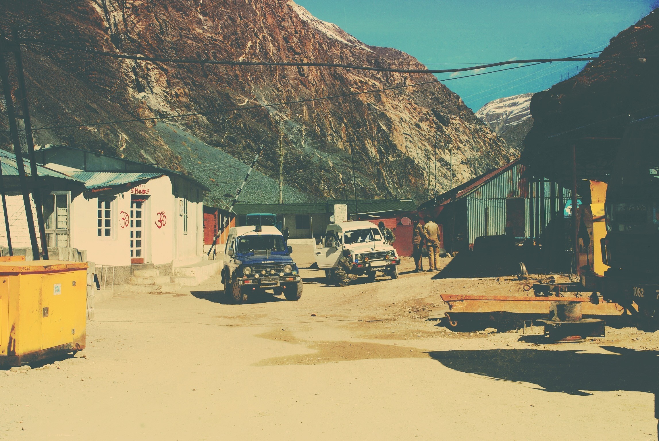 Two SUVs parked in a mountain village with buildings and a generator HD Wallpaper