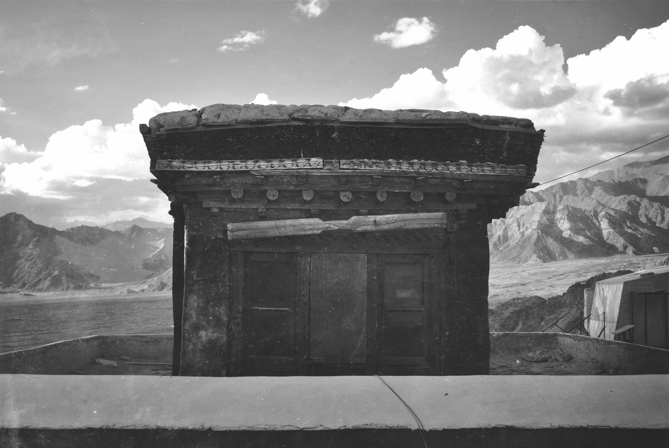 Monochrome photograph of a Tibetan temple structure with mountains in the background HD Wallpaper
