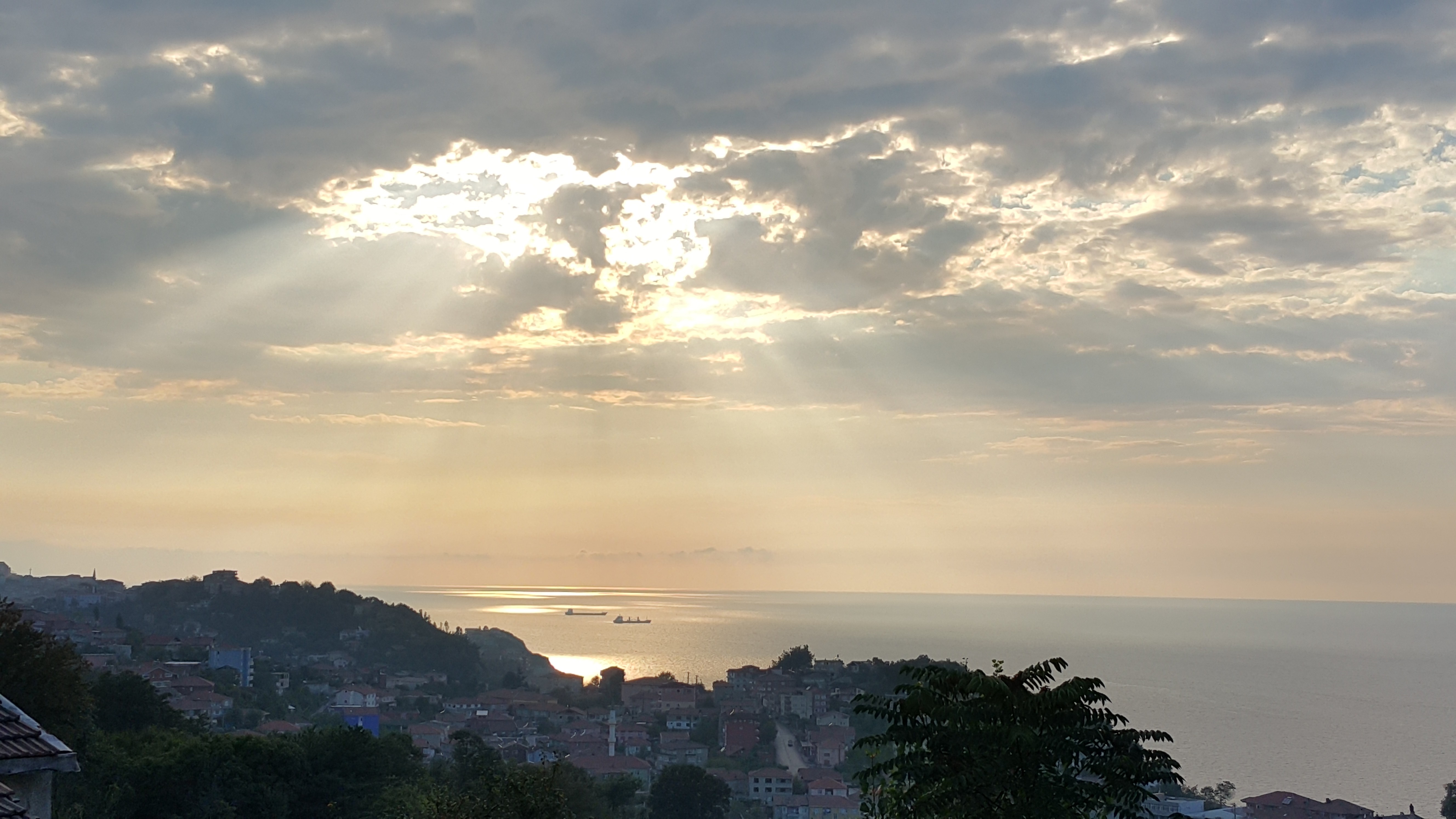 Sunbeams through clouds over a coastal town at sunset HD Wallpaper