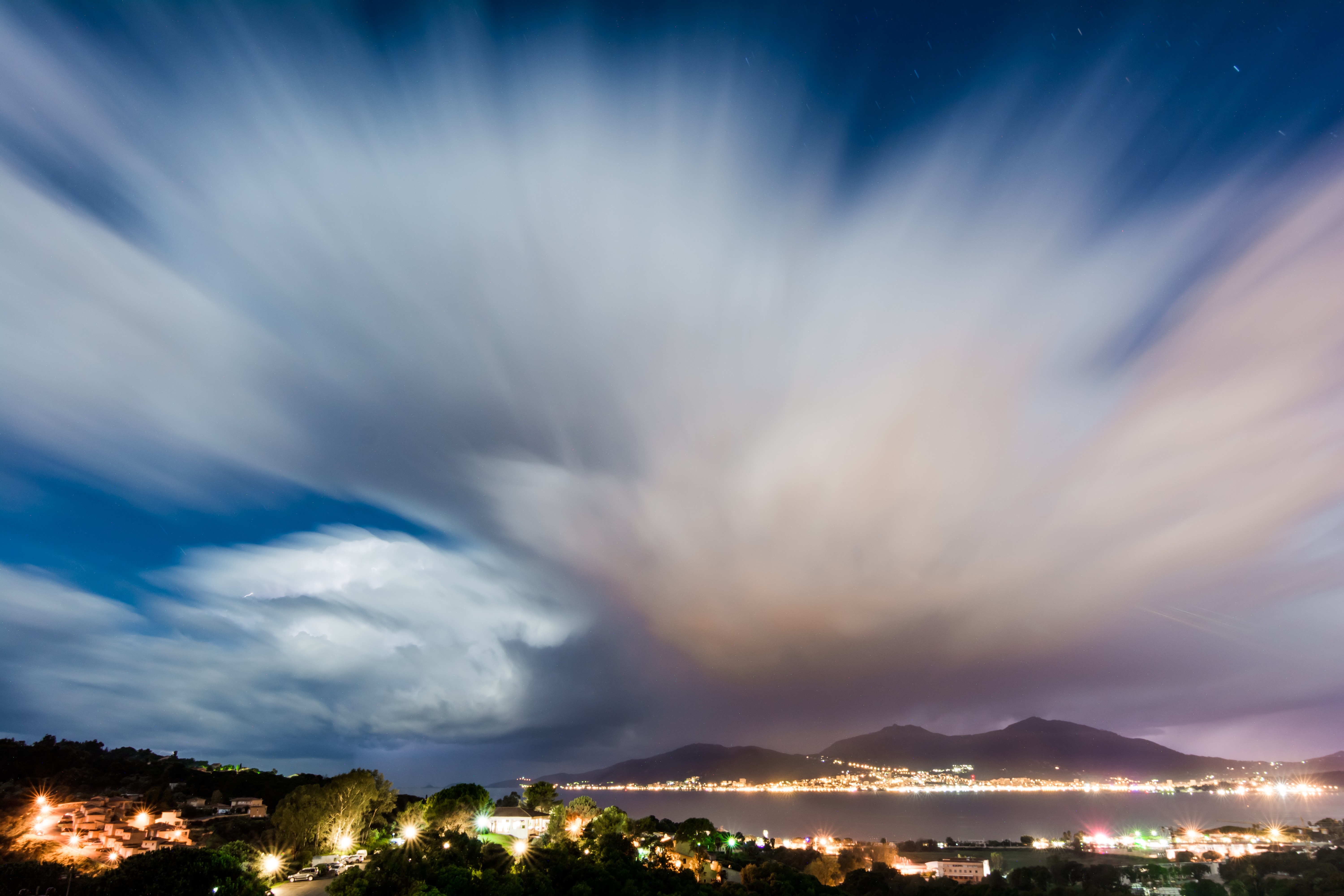 Long exposure clouds over a coastal town at night HD Wallpaper