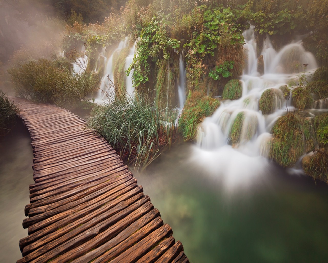 Wooden boardwalk along a misty waterfall in a forest HD Wallpaper
