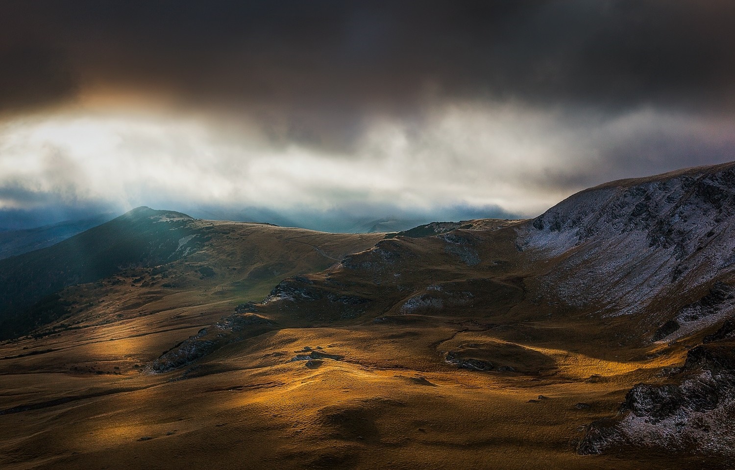 Sunlight breaking through clouds over mountainous terrain HD Wallpaper
