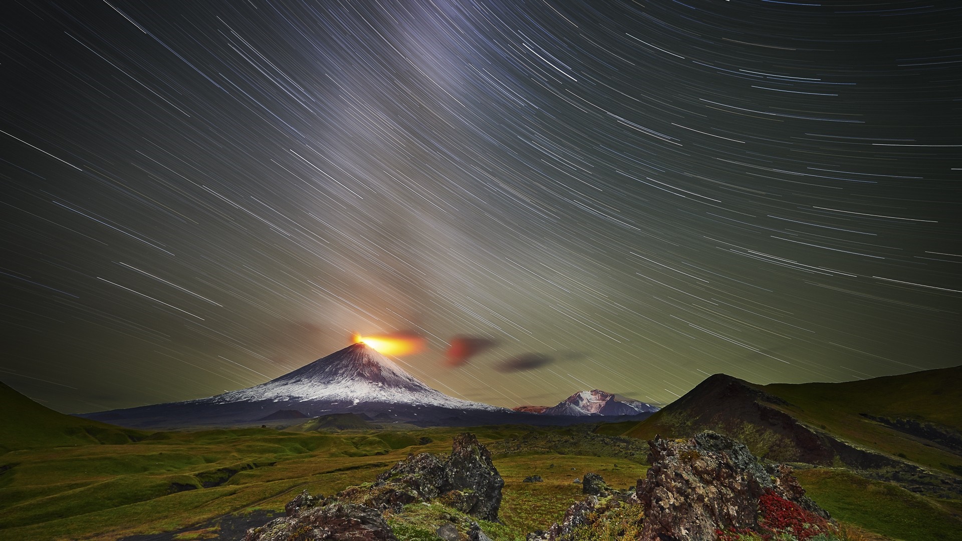 Volcano erupting under star trails at night HD Wallpaper