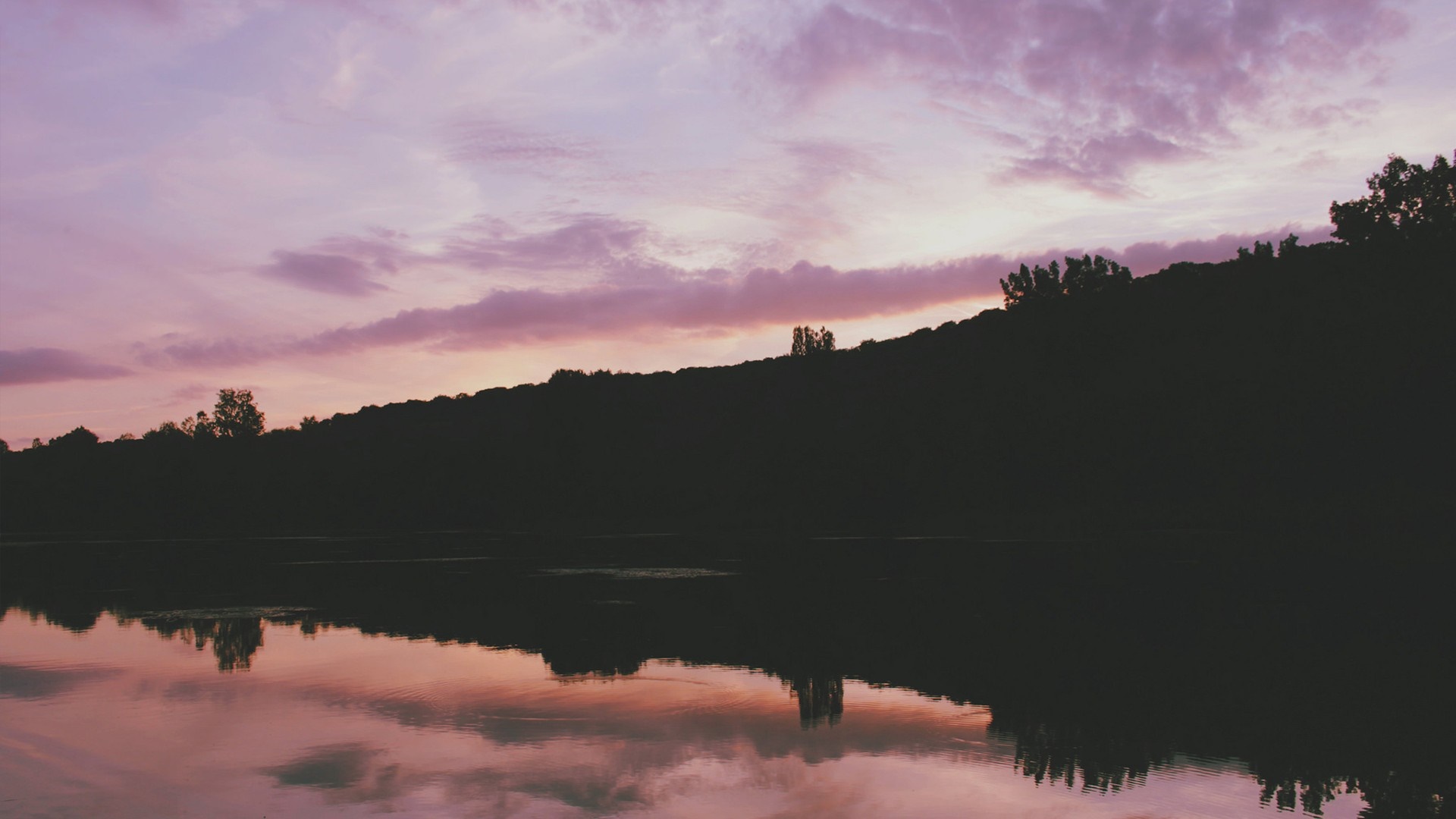 Sunset over a silhouetted hill and lake reflection HD Wallpaper
