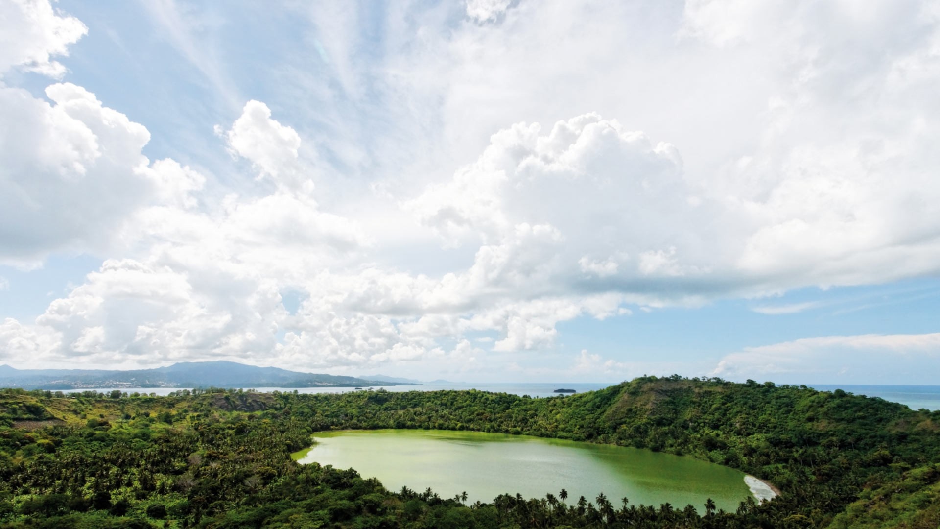 Green lake surrounded by lush forest and hills under cloudy sky HD Wallpaper