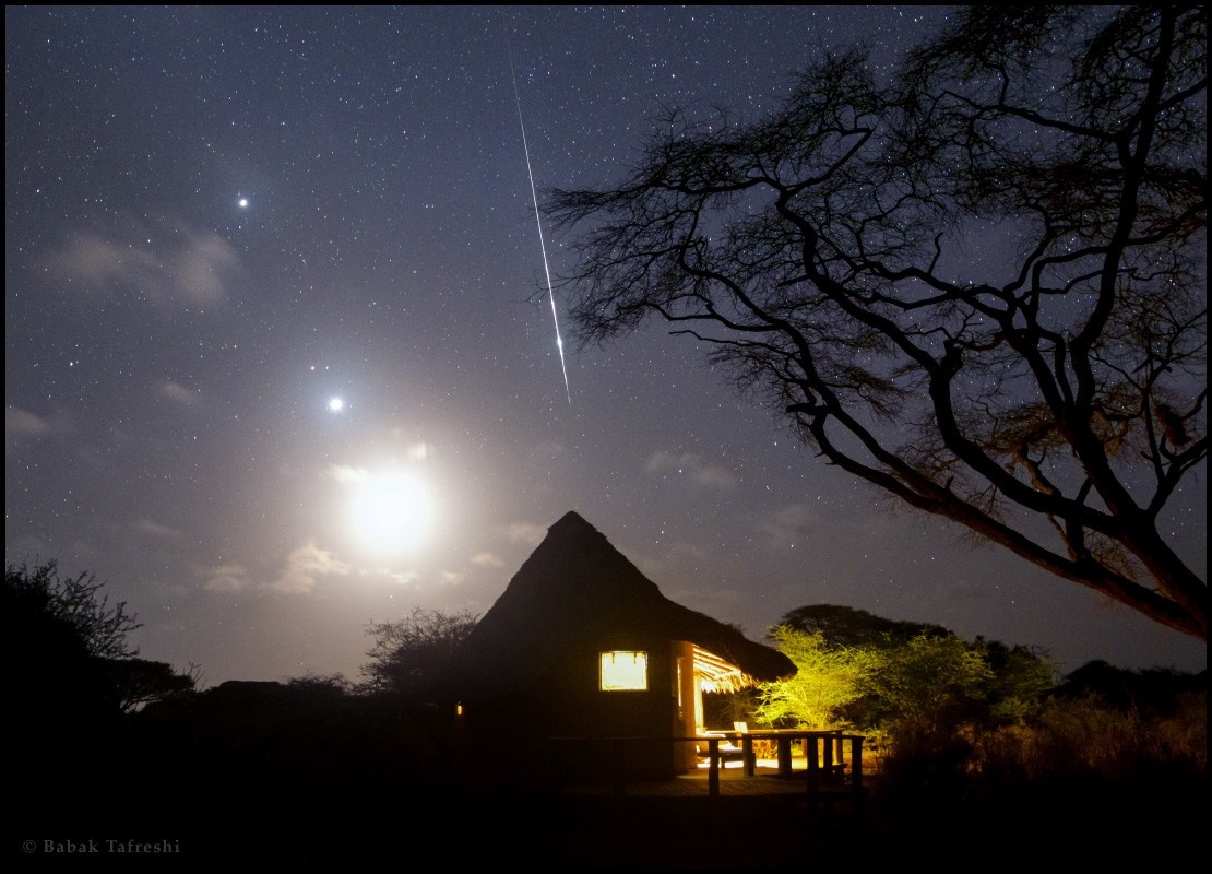 Meteor shower over a thatched hut at night HD Wallpaper