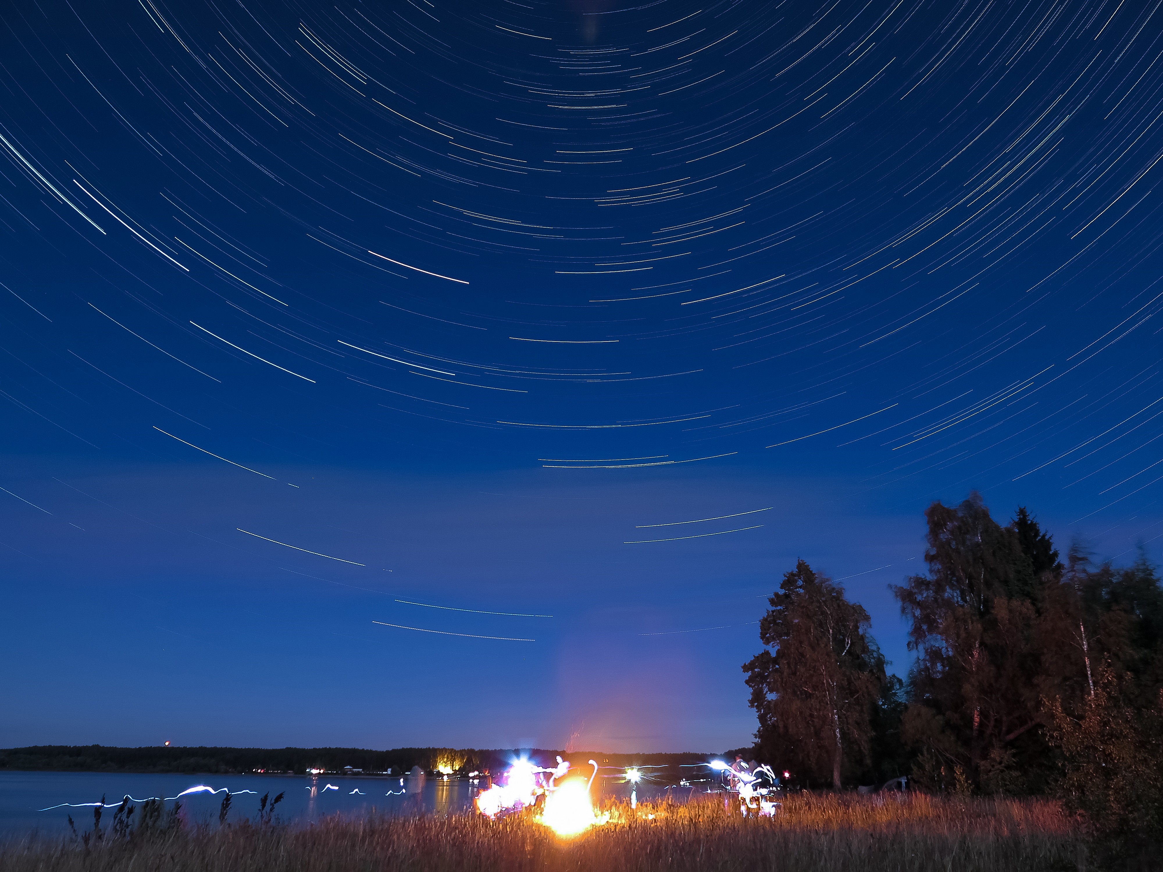 Star trails over a lake with a campfire at night HD Wallpaper