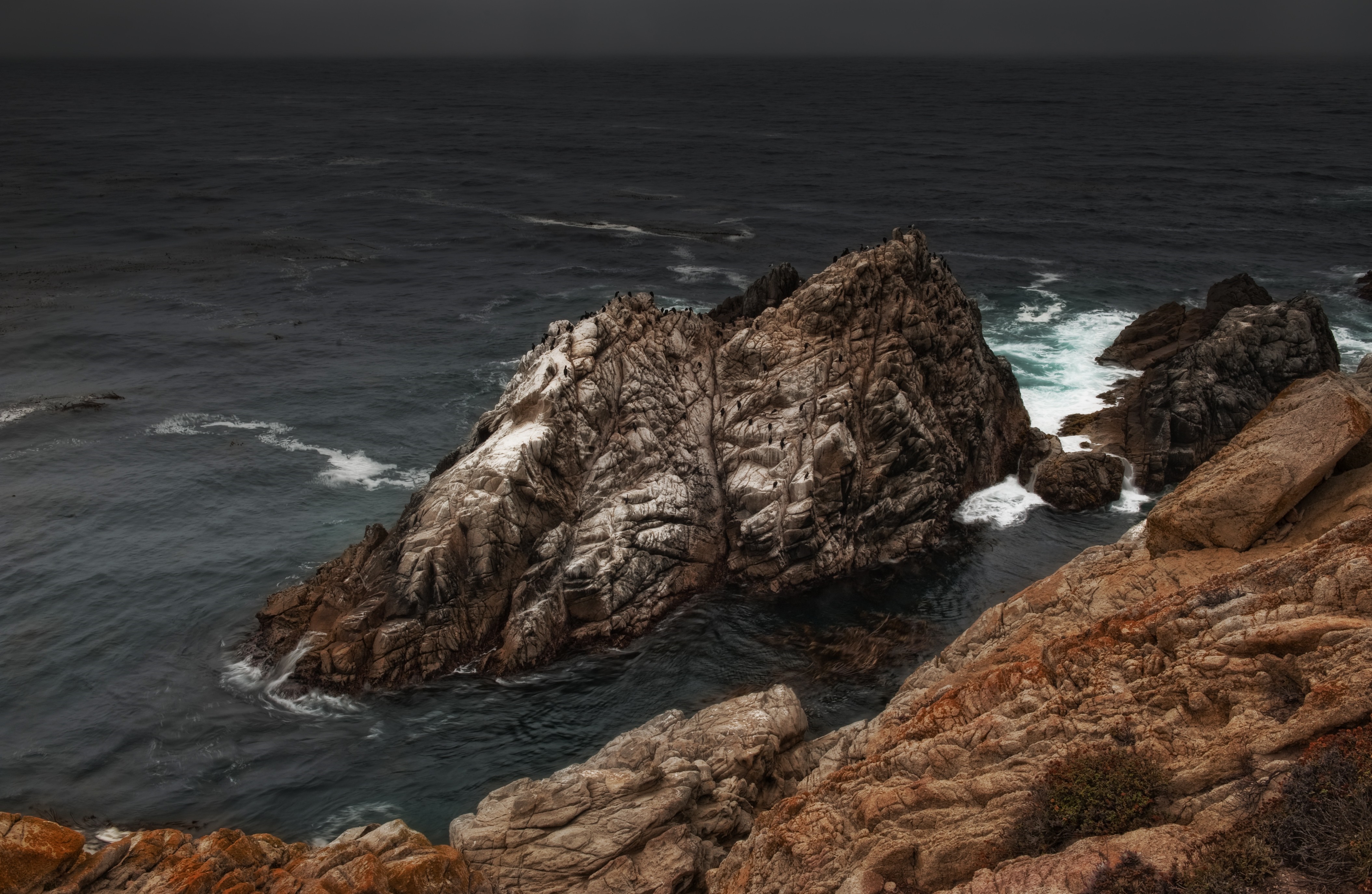 Rocky coast with waves crashing against a large rock formation HD Wallpaper