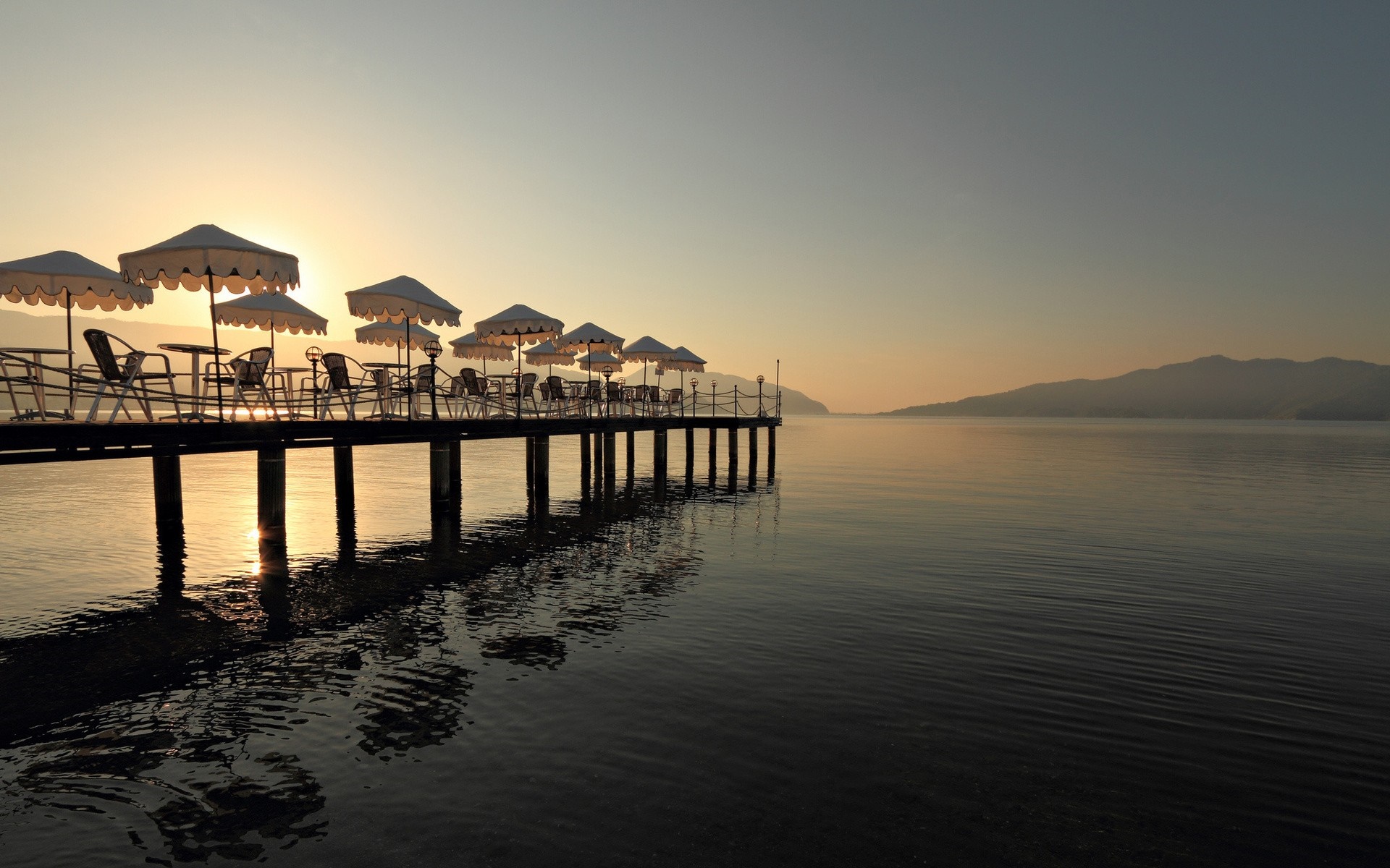 Pier with umbrellas and tables at sunset over the sea HD Wallpaper
