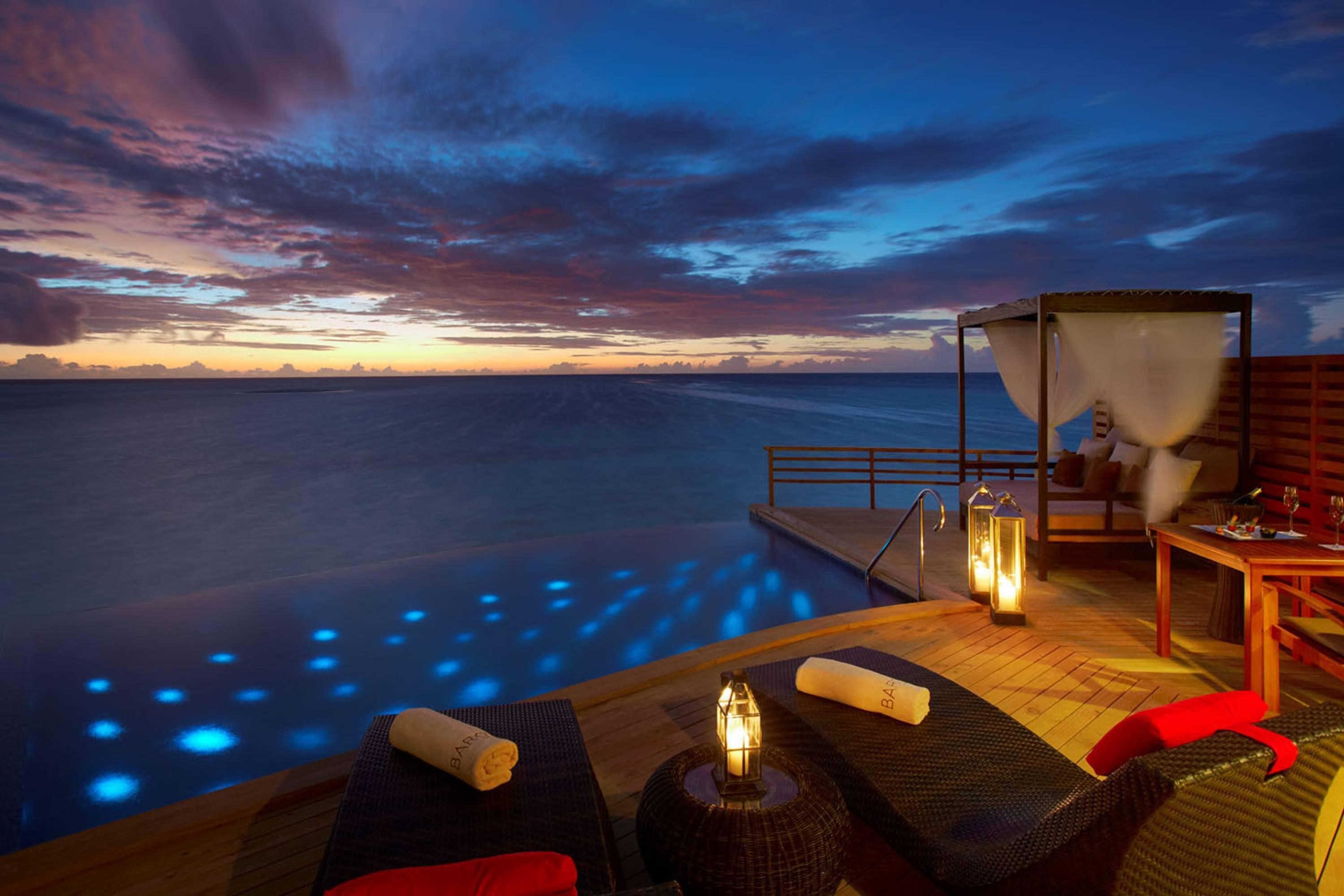 Infinity pool and lounge chairs at sunset over the ocean HD Wallpaper