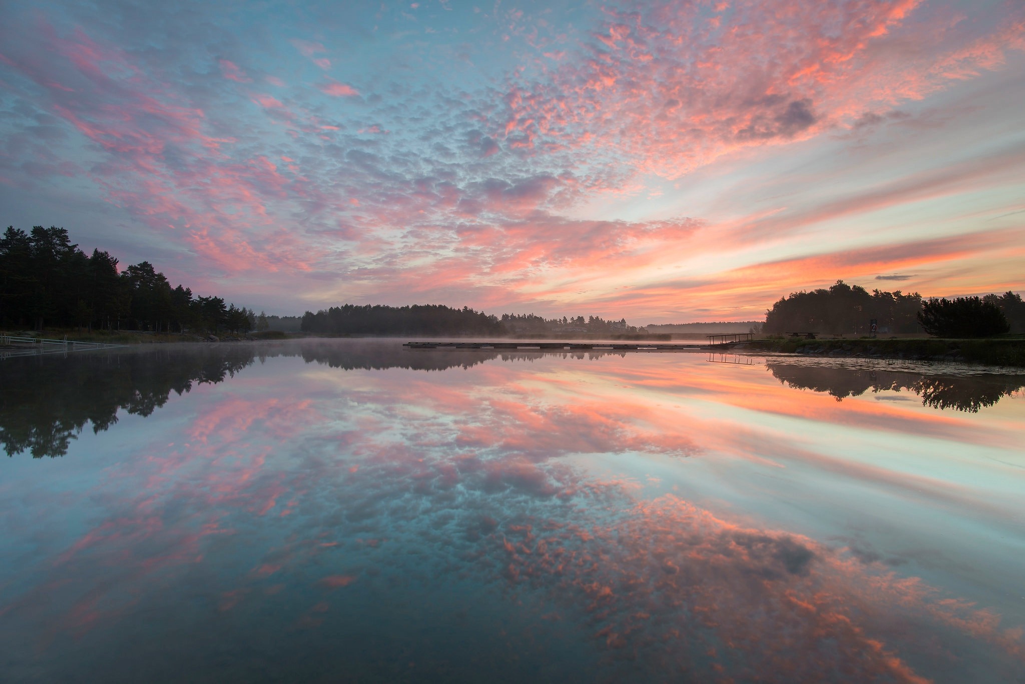 Pink and blue clouds reflected in a calm lake at sunrise or sunset HD Wallpaper