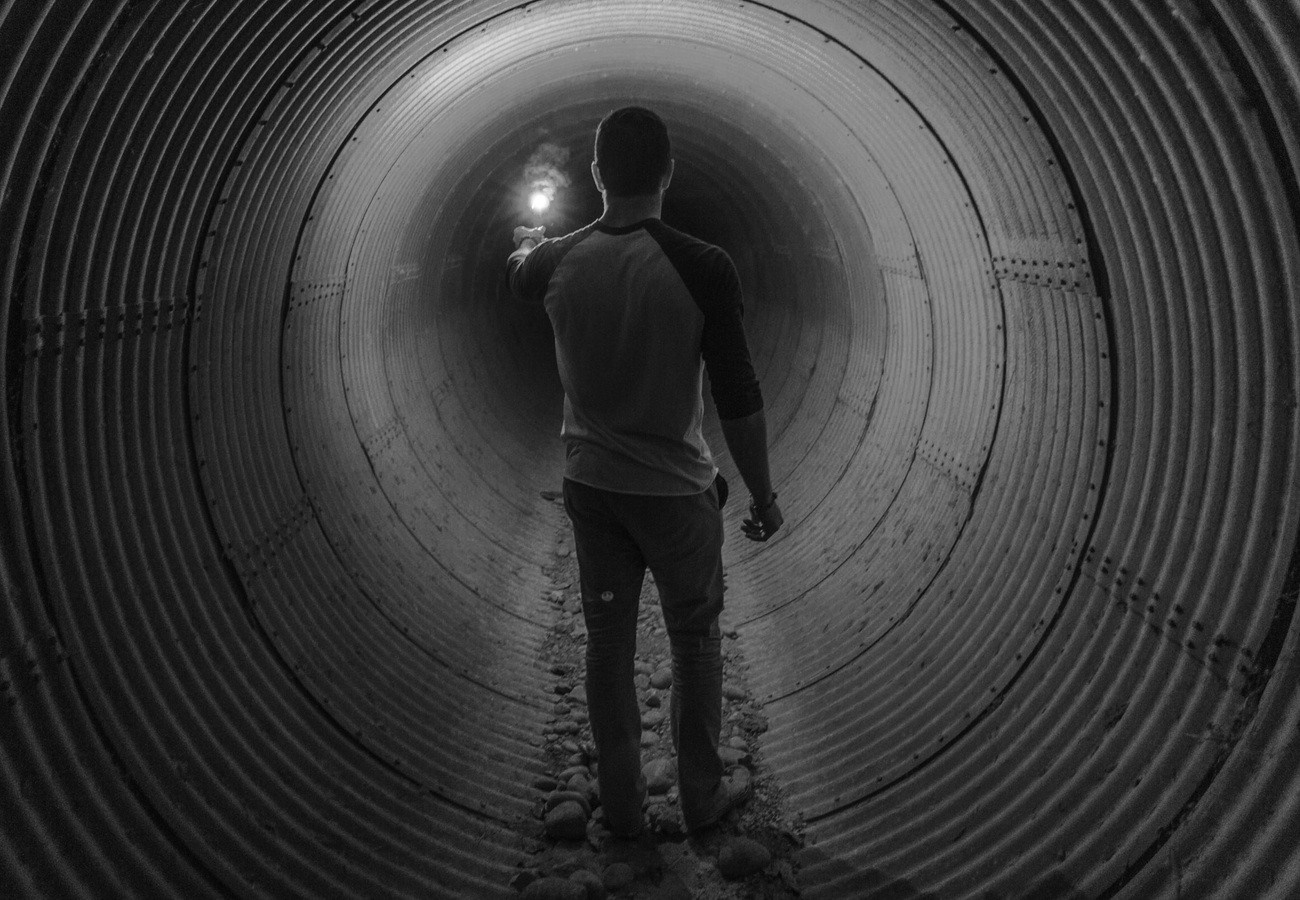 Man holding flashlight in a corrugated metal tunnel HD Wallpaper