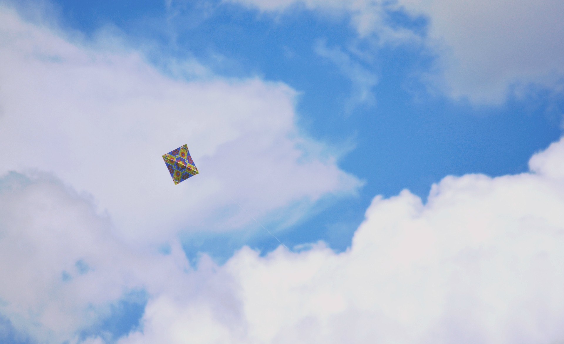 A colorful kite flying in a cloudy blue sky HD Wallpaper