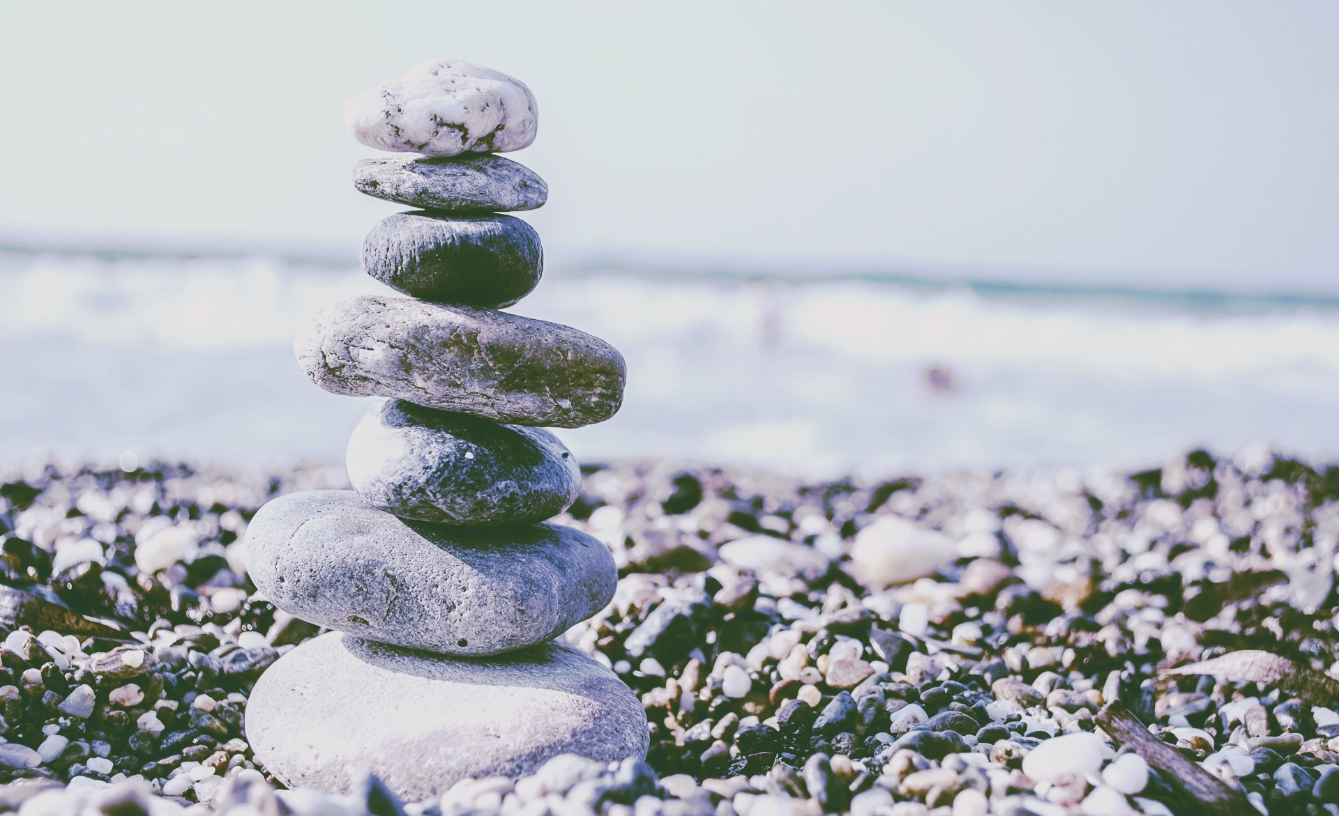 Stack of stones on a beach with ocean waves HD Wallpaper