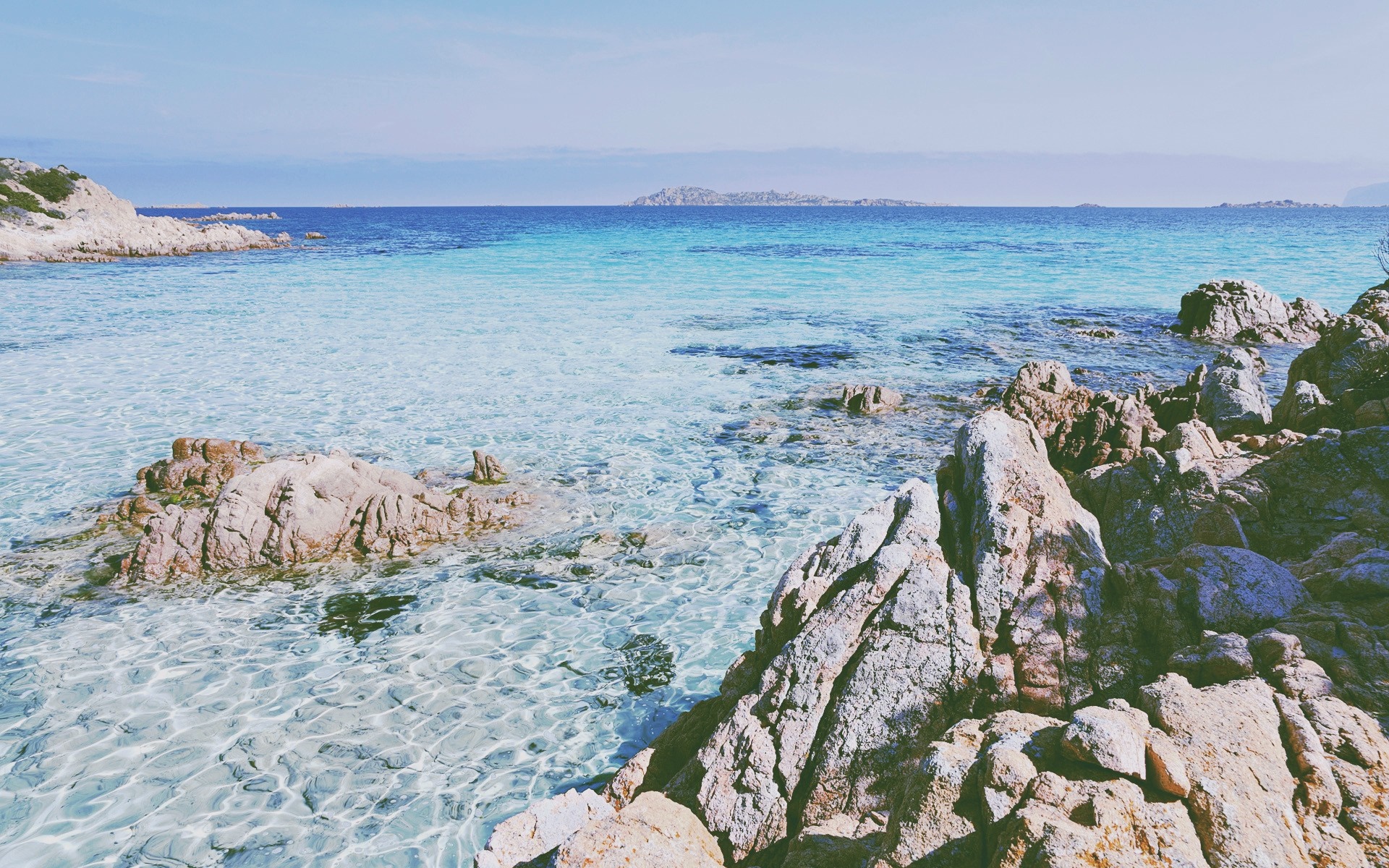 Rocky coastline with clear turquoise water and distant islands HD Wallpaper