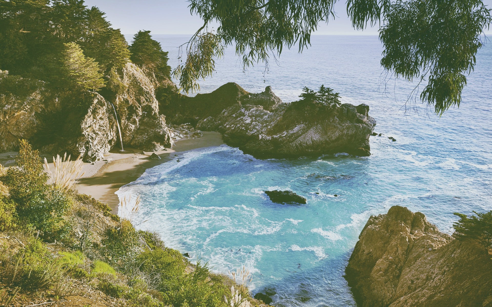 Waterfall cascading into a turquoise cove on a rocky coastline HD Wallpaper