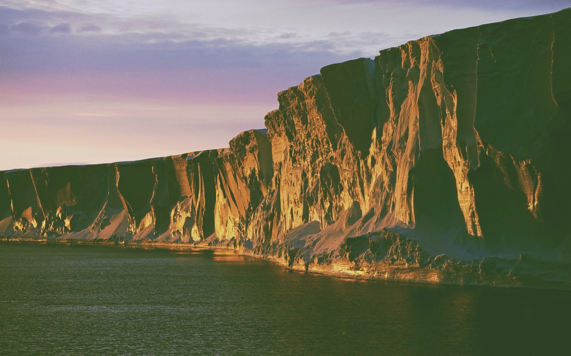 Cliff face illuminated by sunset over the ocean HD Wallpaper