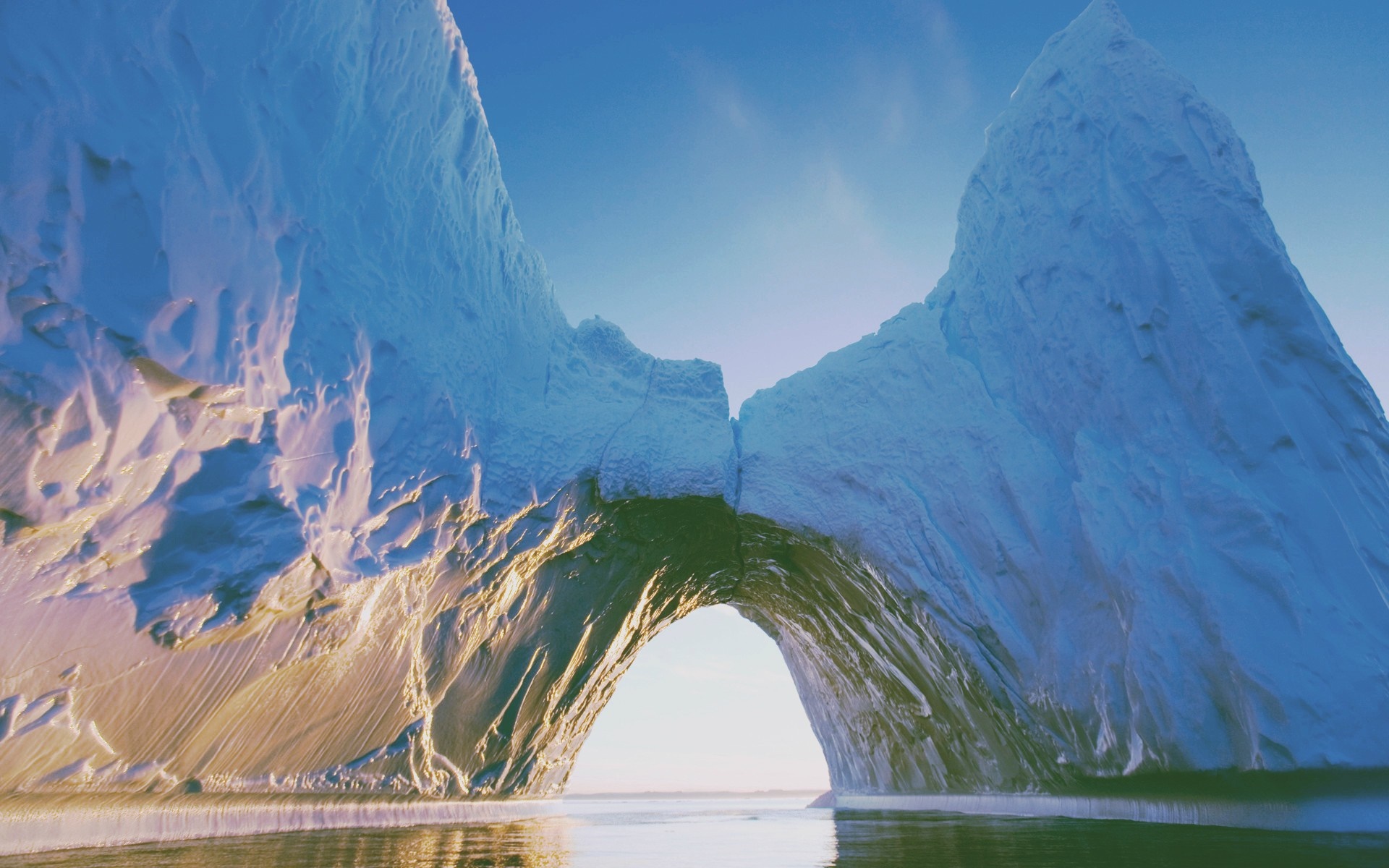 Iceberg arch over calm water under blue sky HD Wallpaper