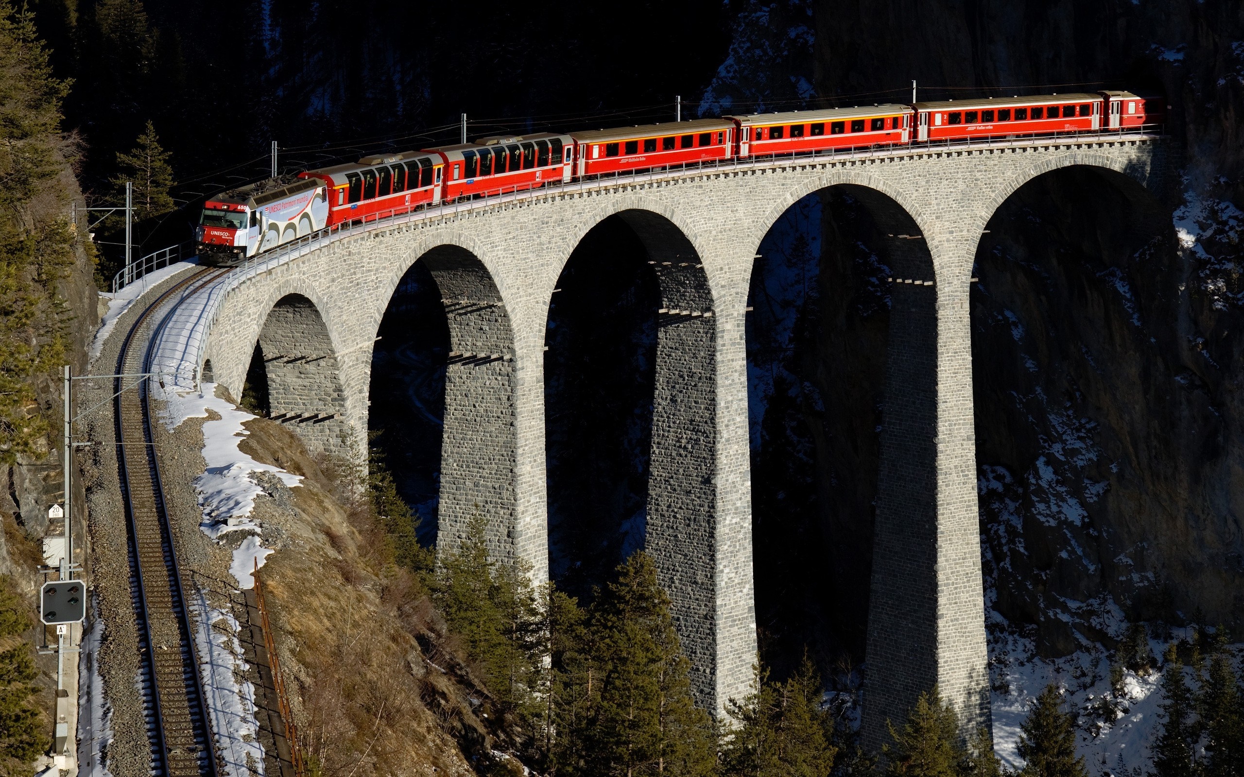 Red train crossing a stone viaduct bridge in Switzerland HD Wallpaper