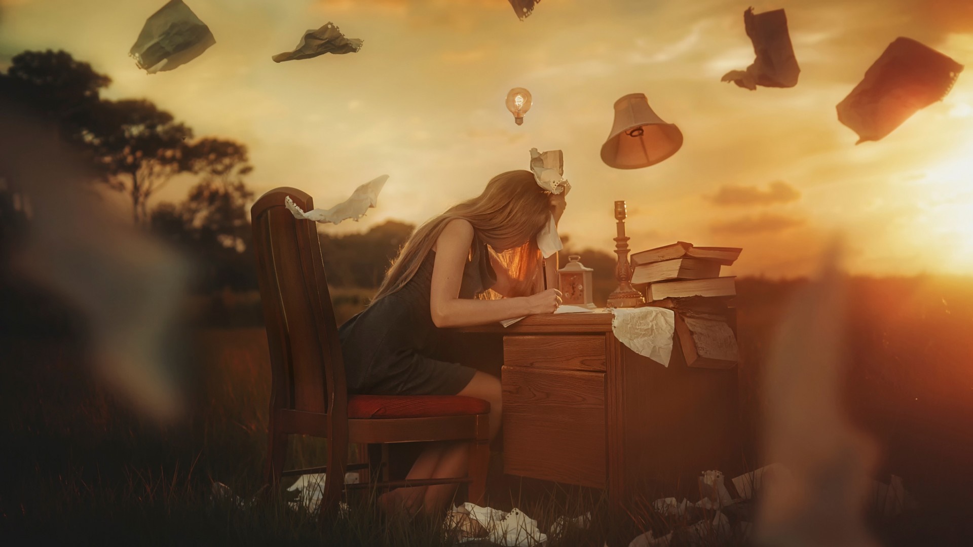 Woman studying at a desk in a field at sunset HD Wallpaper