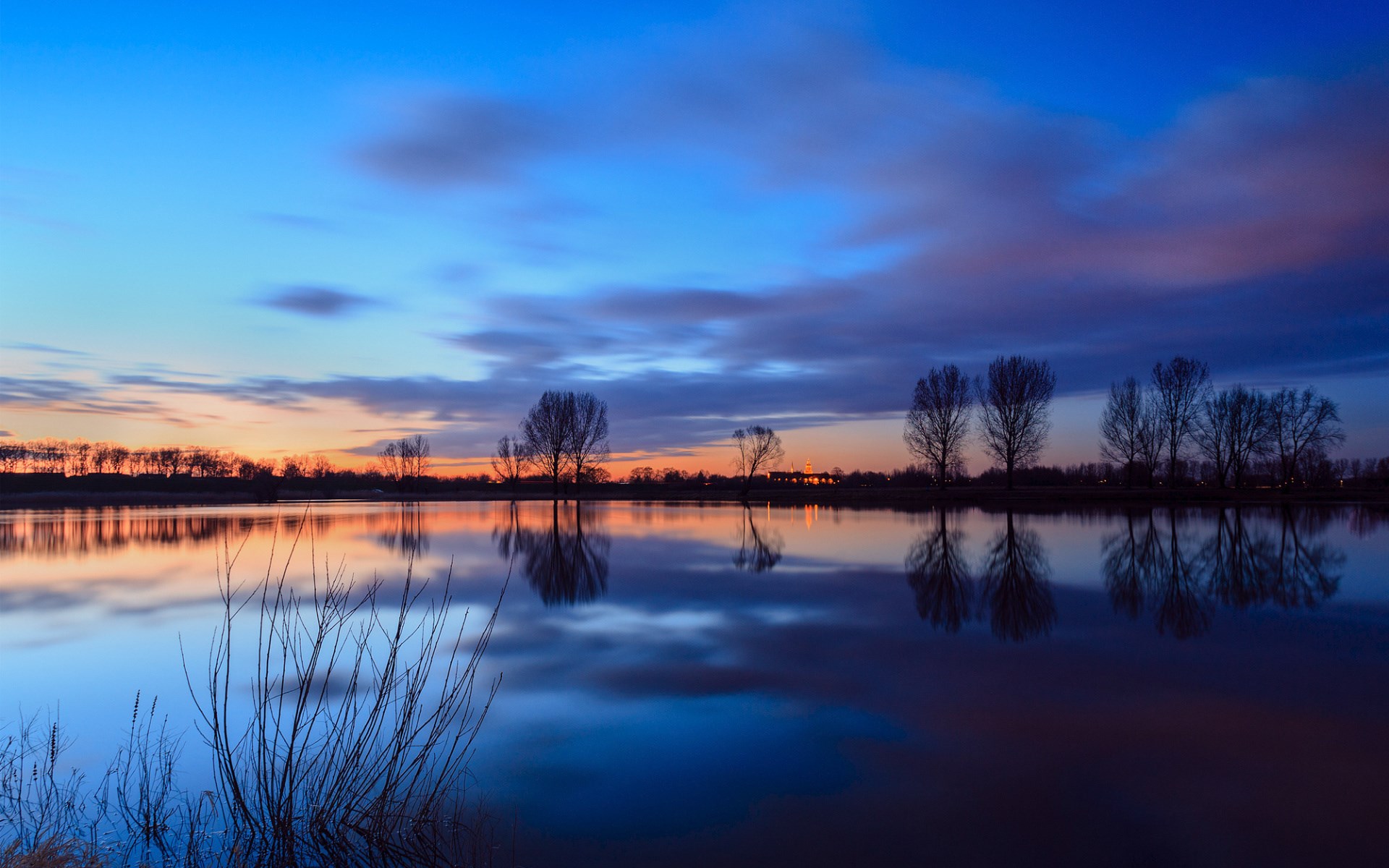 Sunset over a calm lake with silhouetted trees HD Wallpaper