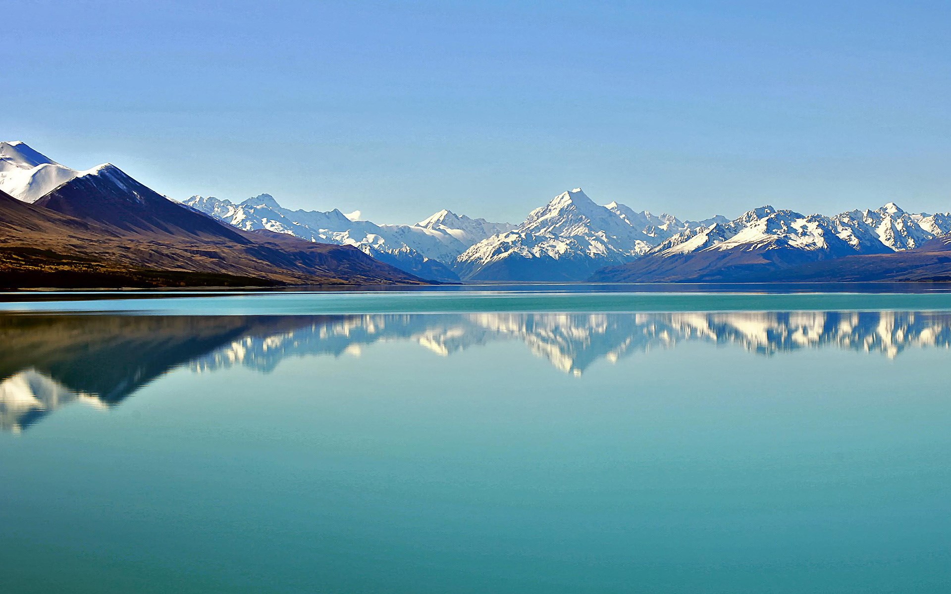 Snow-capped mountains reflected in a turquoise lake HD Wallpaper