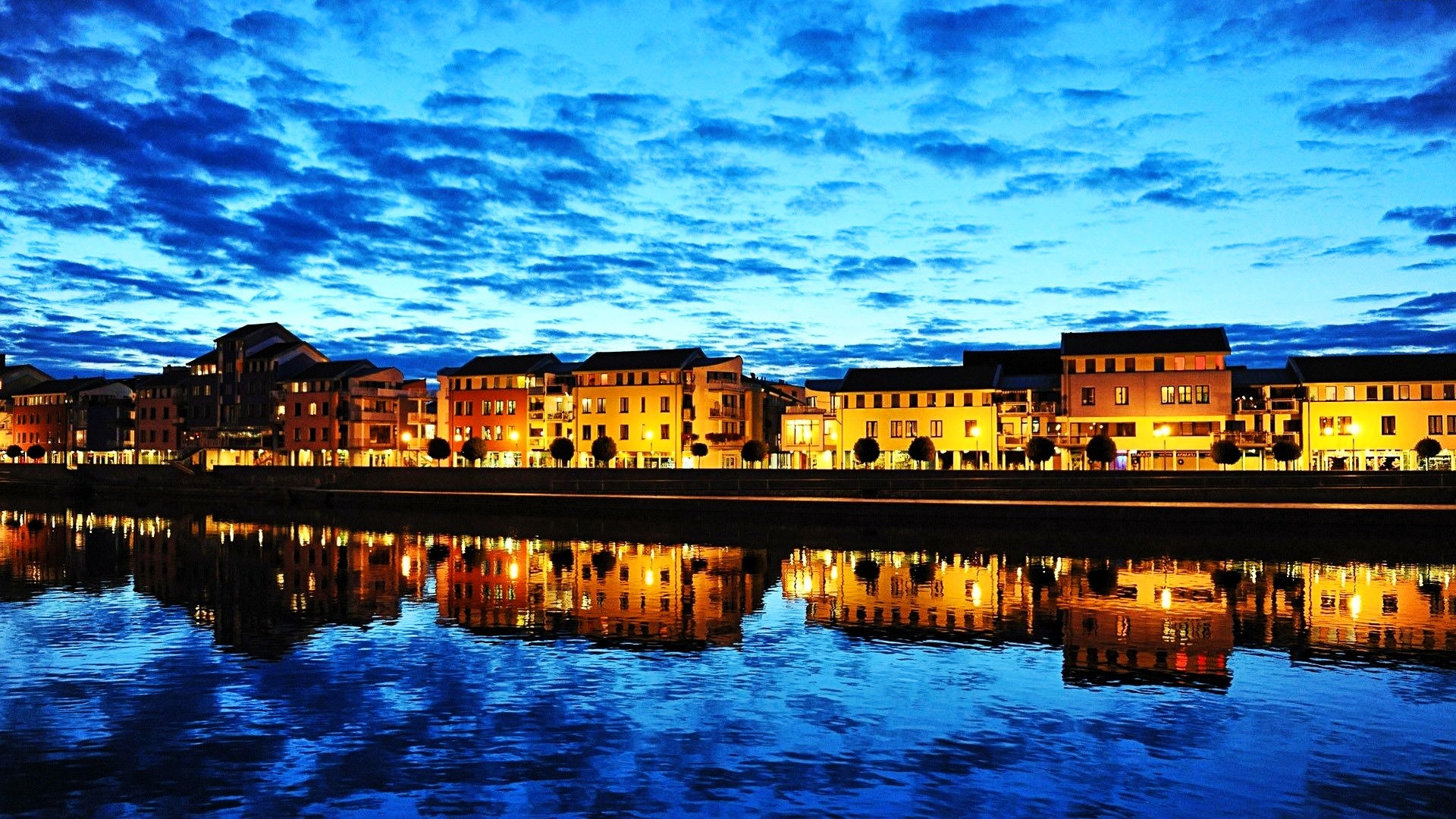 Cityscape with buildings reflecting in a river at dusk HD Wallpaper