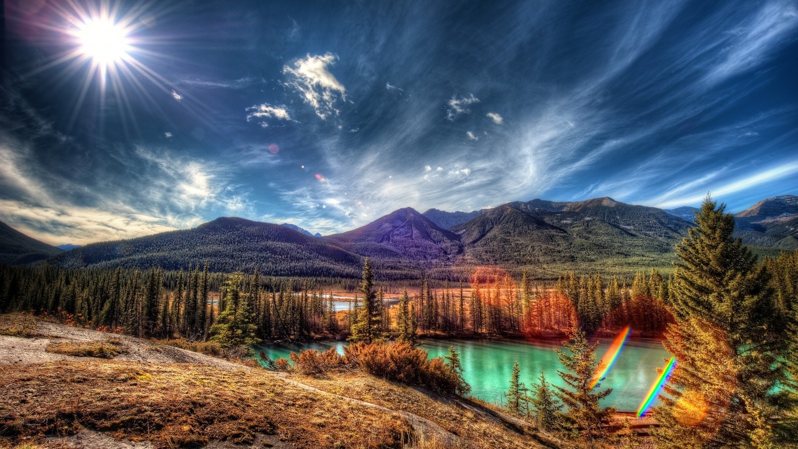 Sunlight over a mountain range and forest with a turquoise river HD Wallpaper