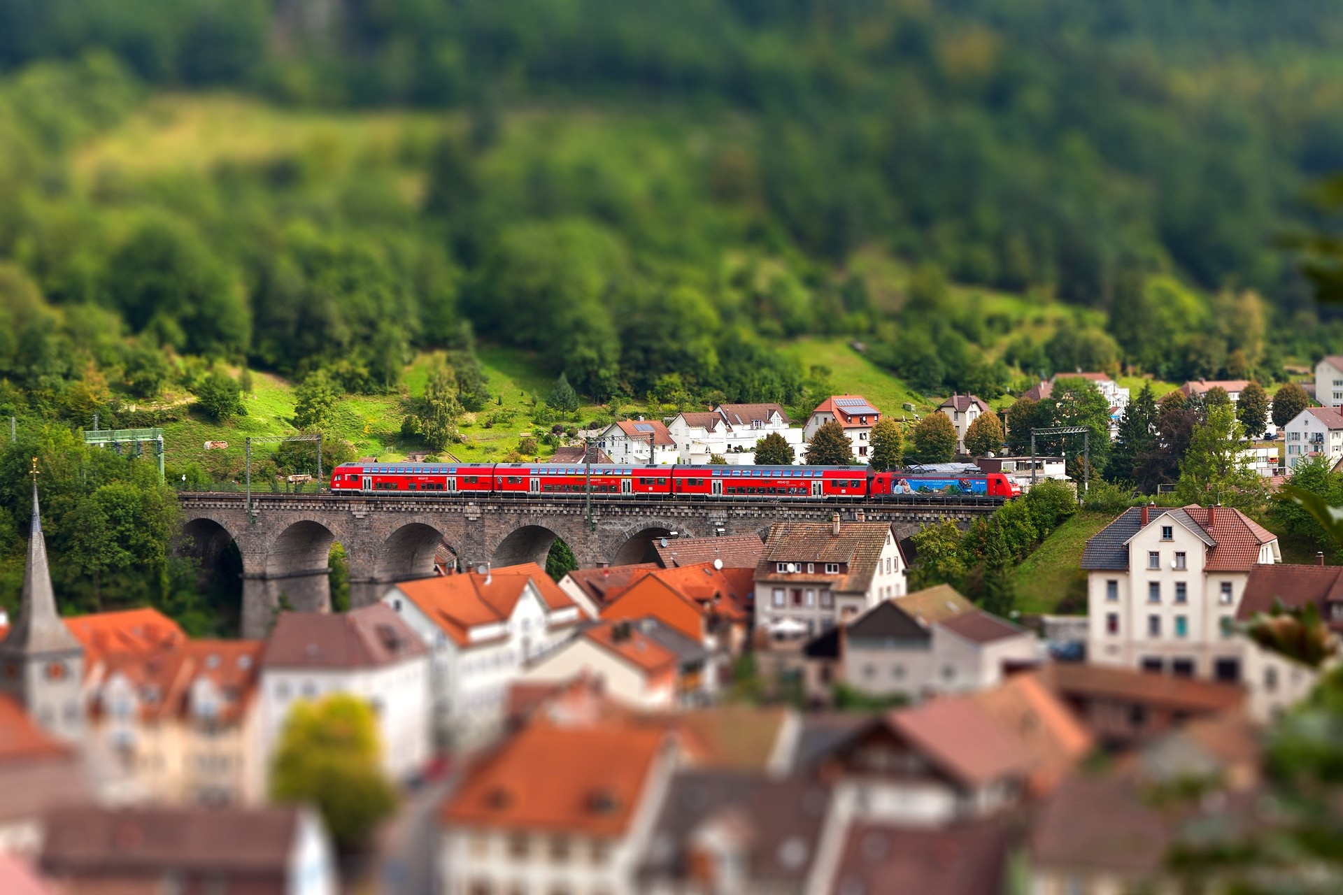 Red train on a bridge over a river in a town HD Wallpaper