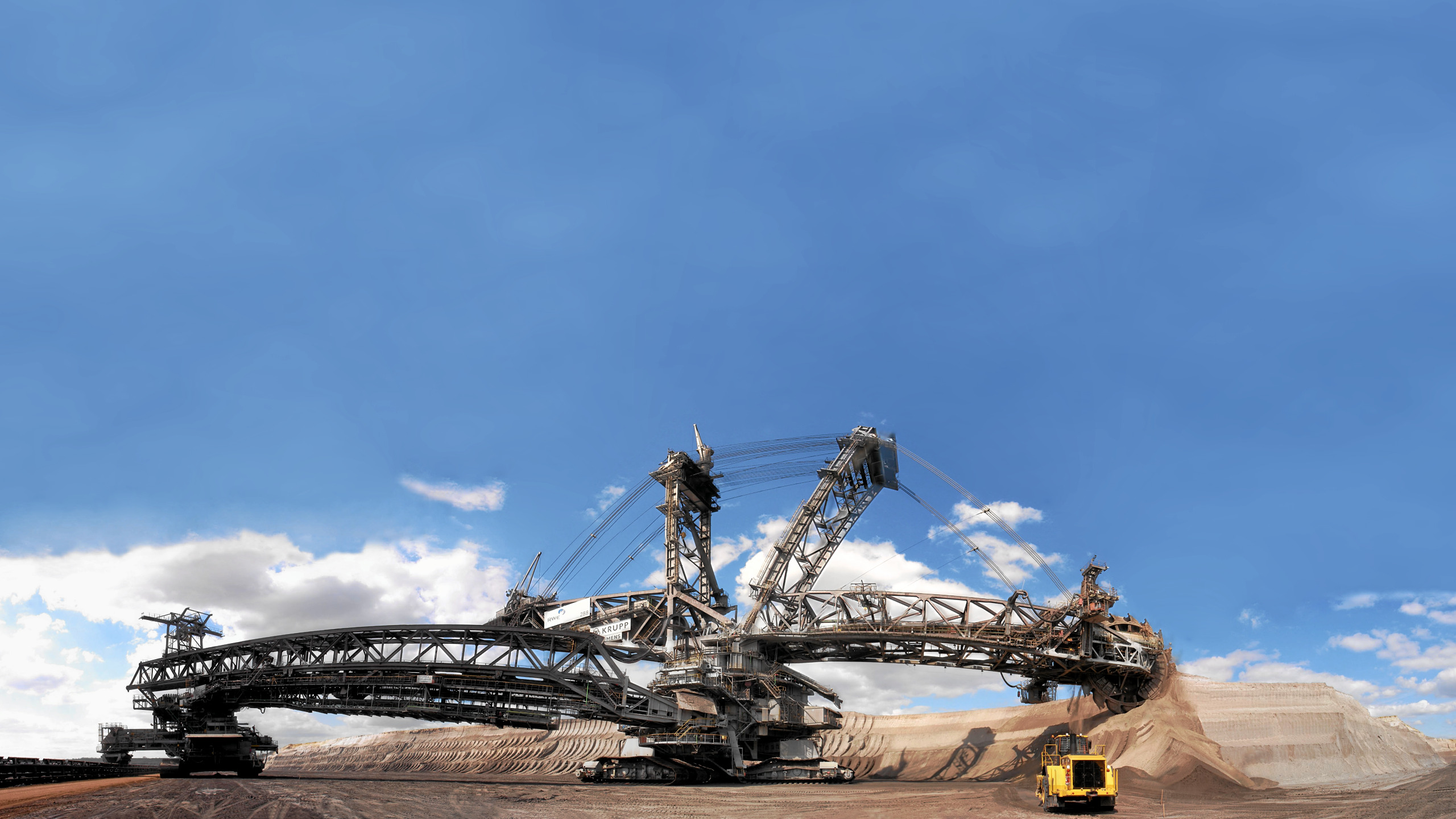 Giant bucket-wheel excavator in a mine under blue sky HD Wallpaper