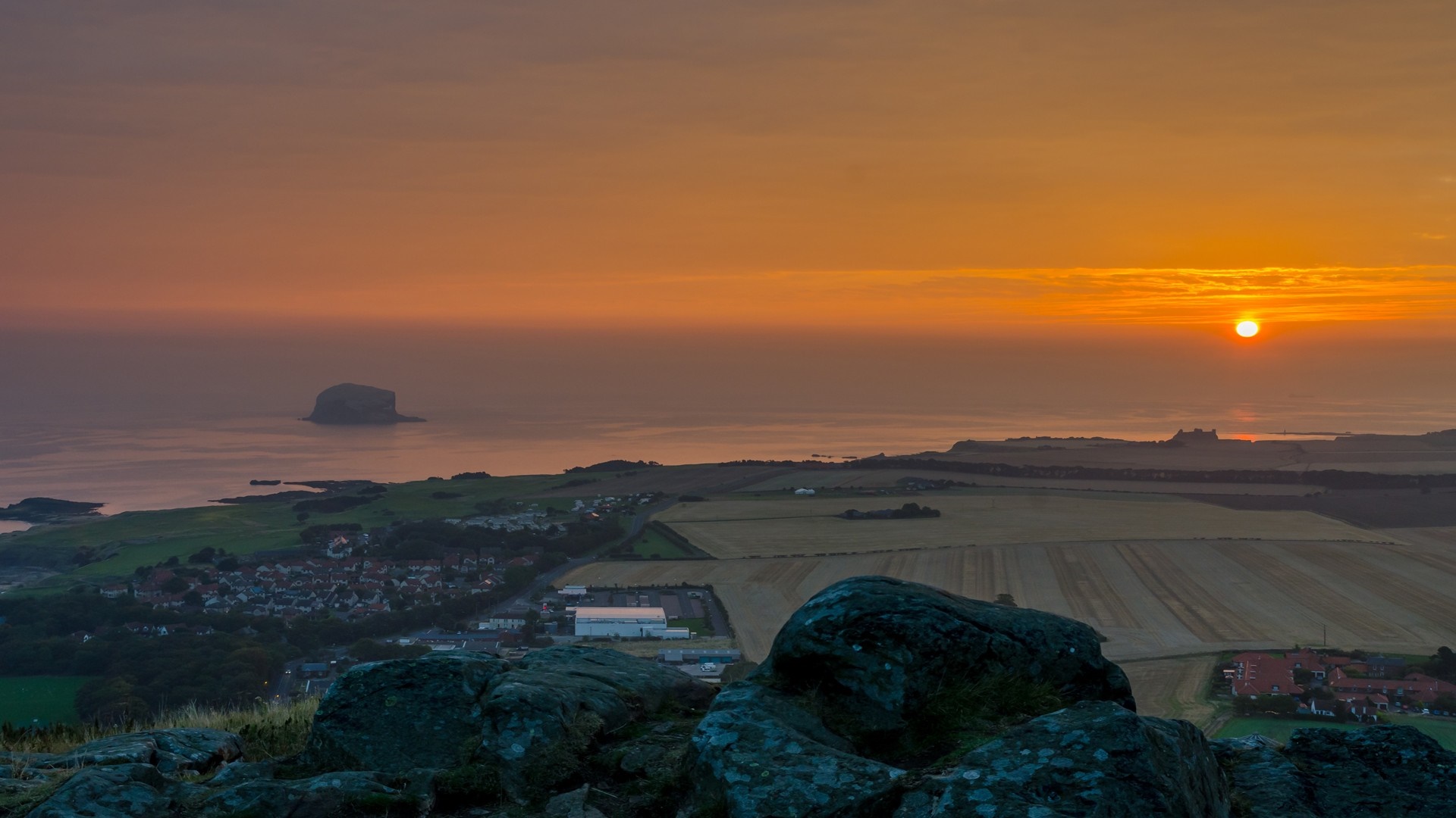 Sunset over the sea with a coastal town and island HD Wallpaper