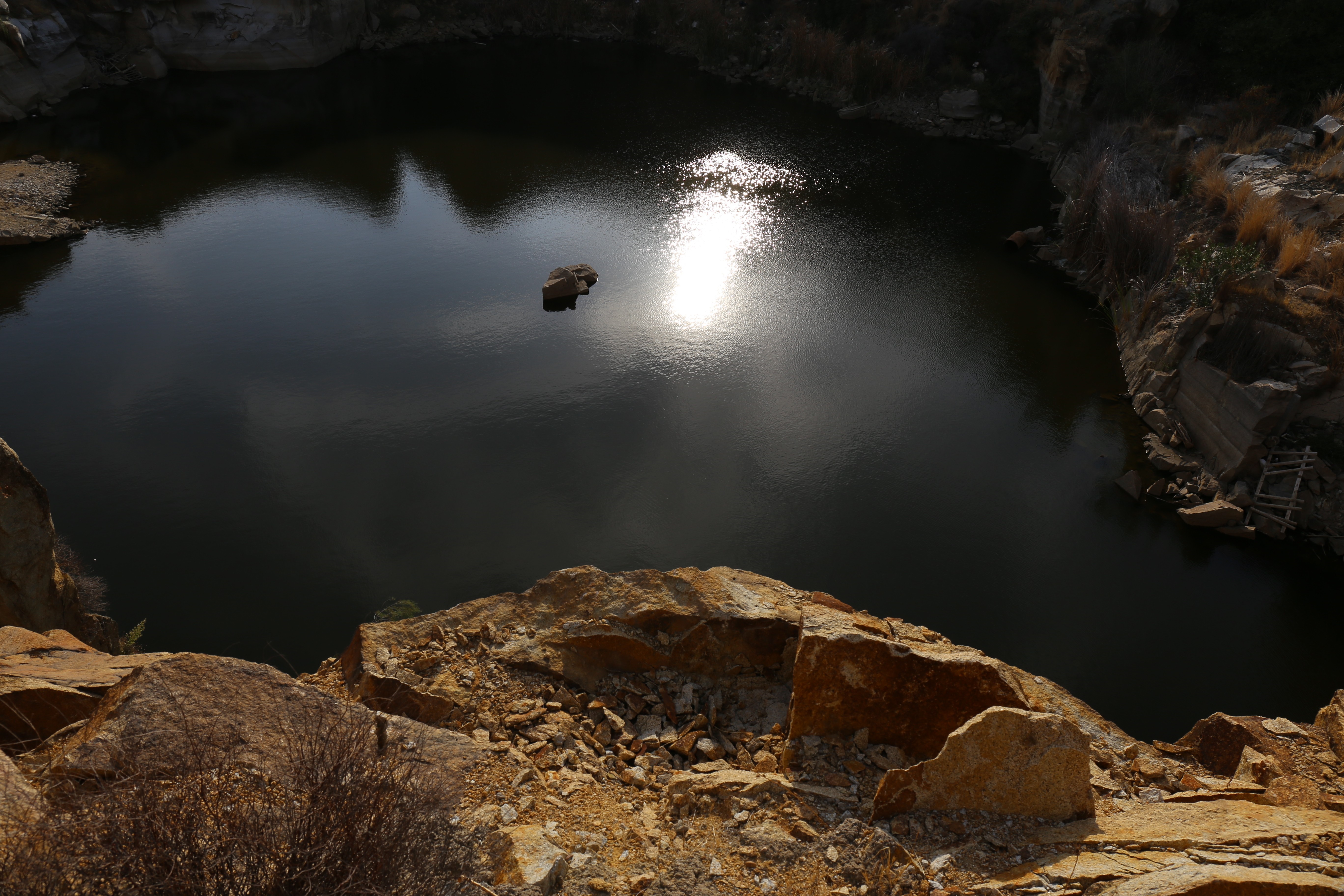 Rocky quarry lake with sun reflection and a single rock HD Wallpaper