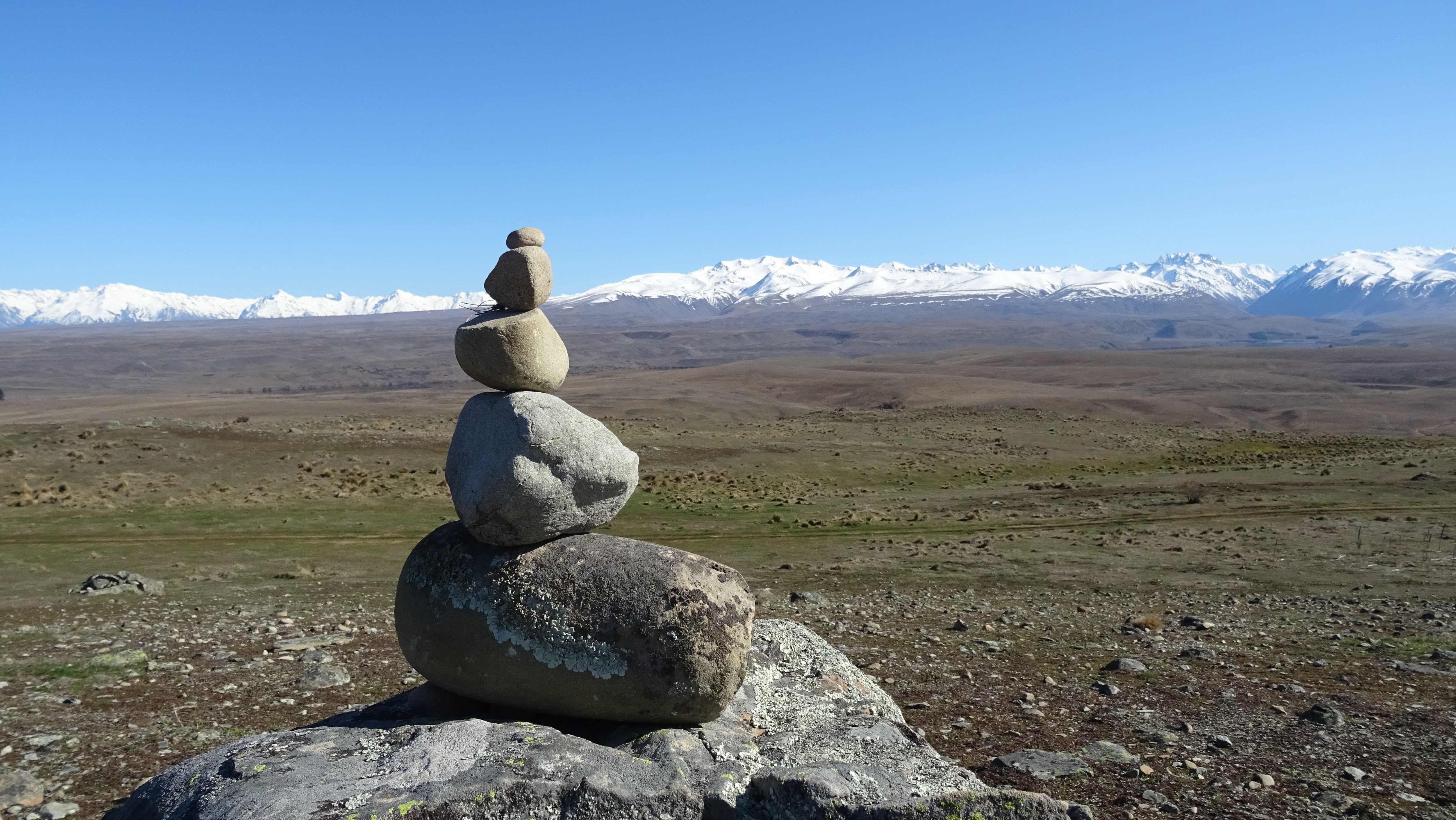 Stone cairn in front of snow-capped mountains in New Zealand HD Wallpaper
