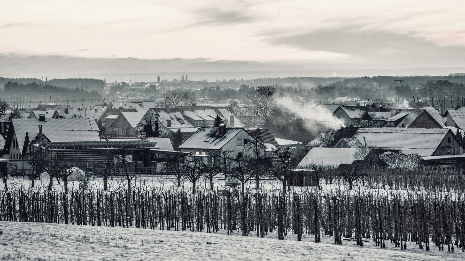 Snowy village with smoke rising from chimneys in winter HD Wallpaper