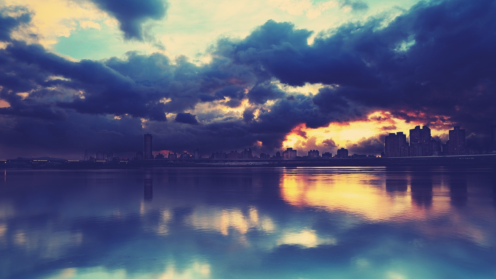 City skyline reflected in water at sunset with dramatic clouds HD Wallpaper
