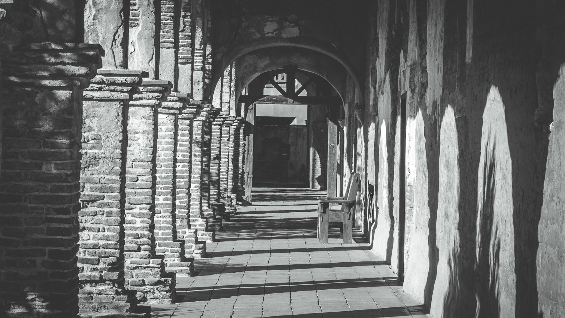 Monochrome photograph of an ancient arched hallway with columns HD Wallpaper