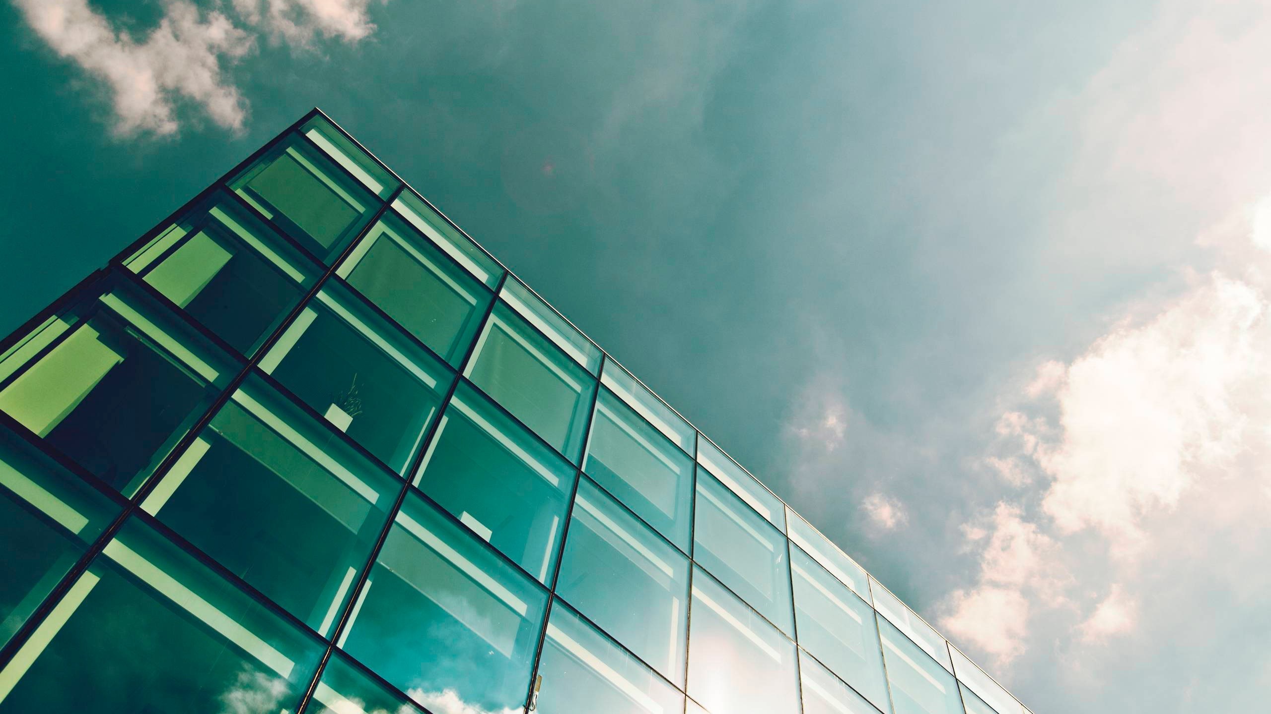 Modern glass building facade against a cloudy sky HD Wallpaper