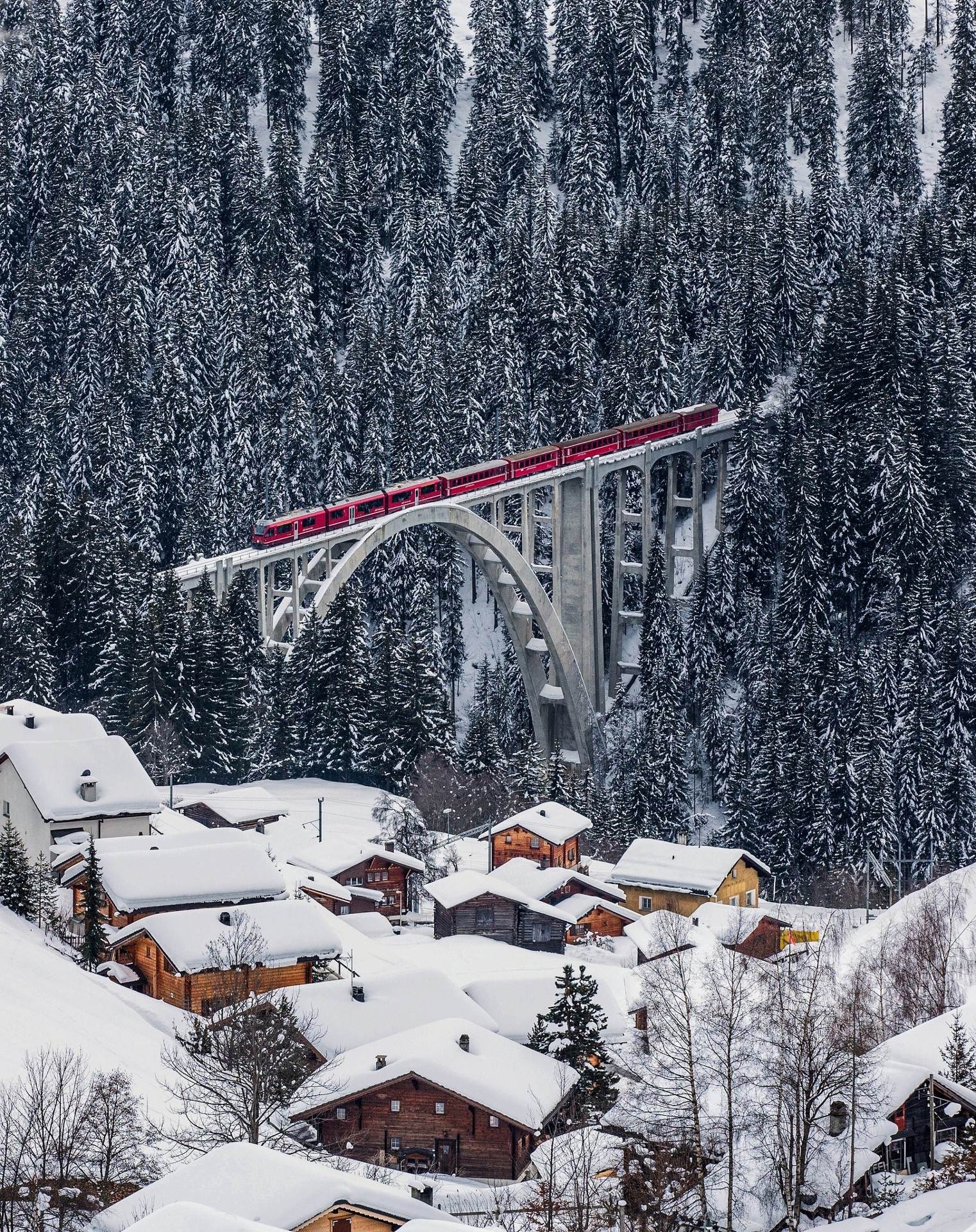 Red train crossing a snowy bridge in Switzerland HD Wallpaper