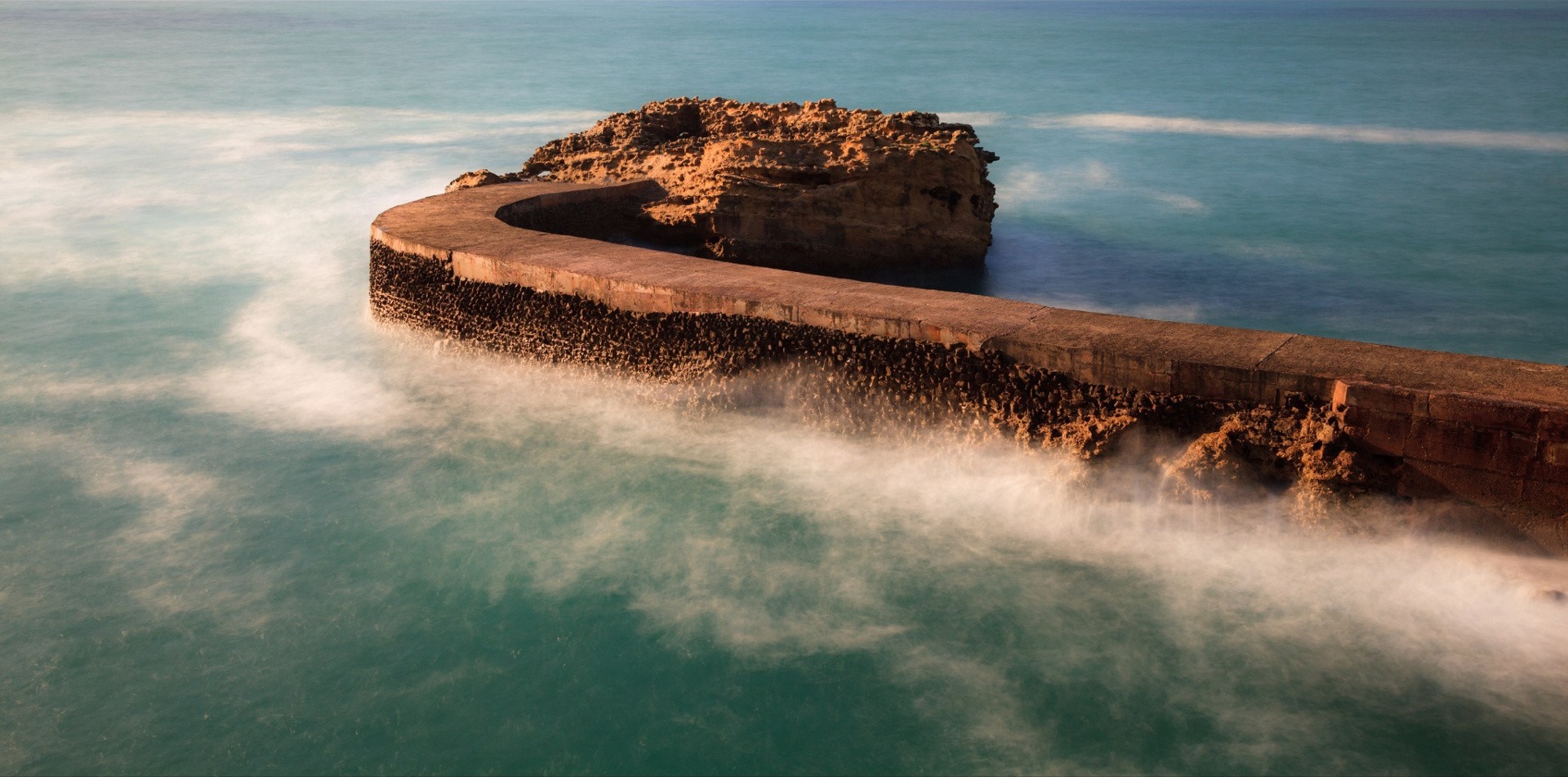 Curved breakwater and rock formation in the sea HD Wallpaper
