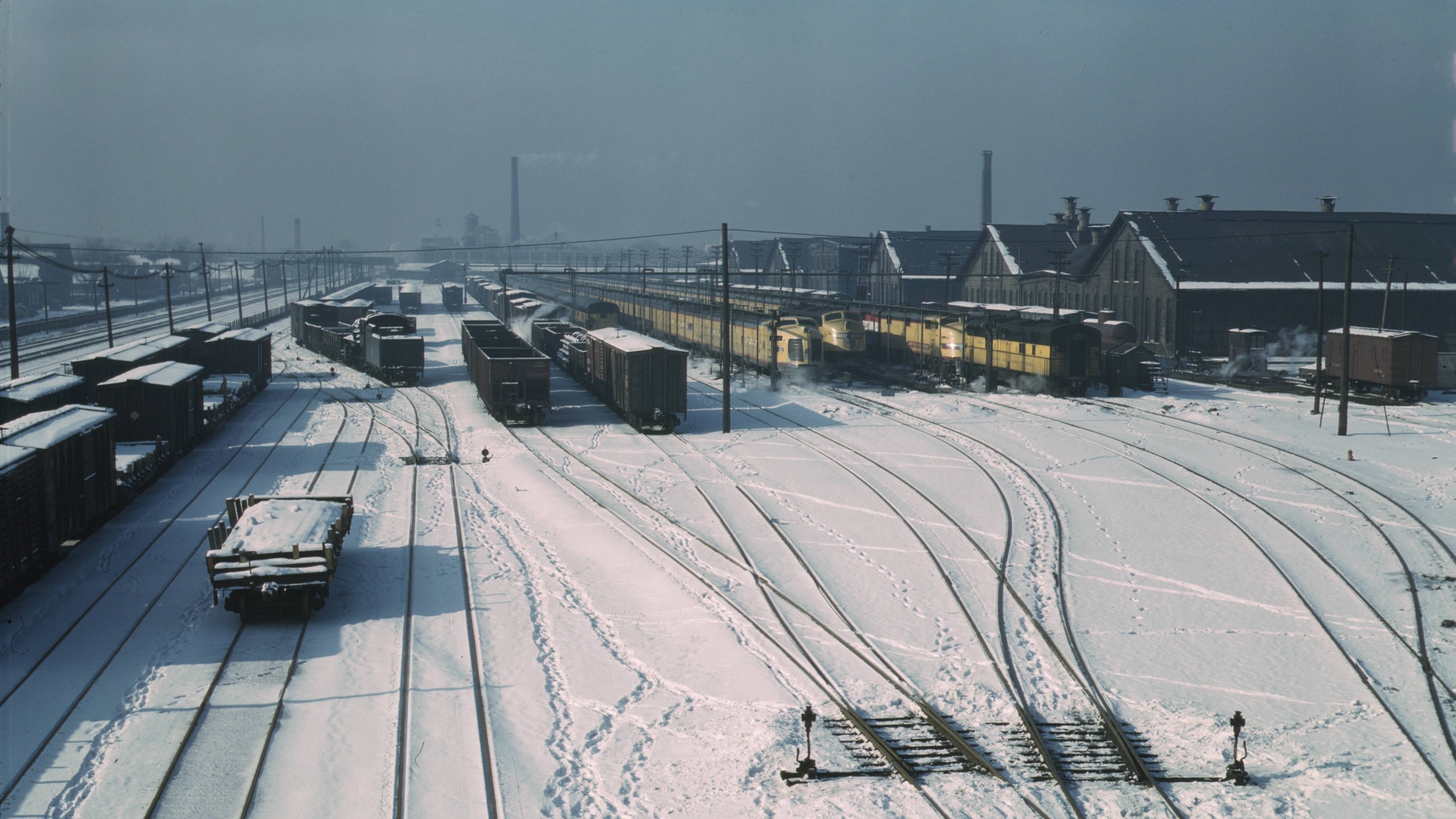 Snowy train yard with freight trains and buildings HD Wallpaper