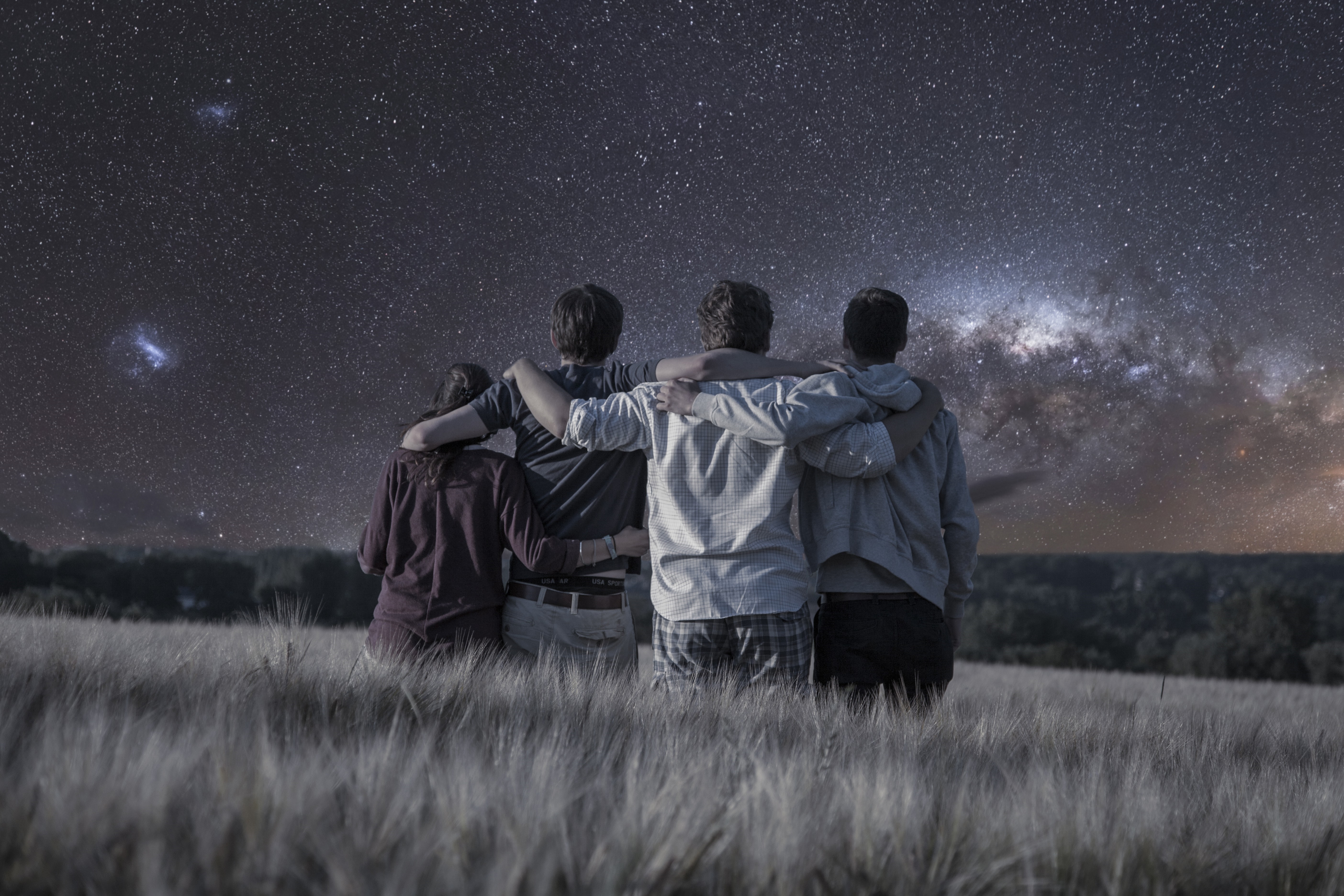 Four friends embracing under a starry night sky HD Wallpaper