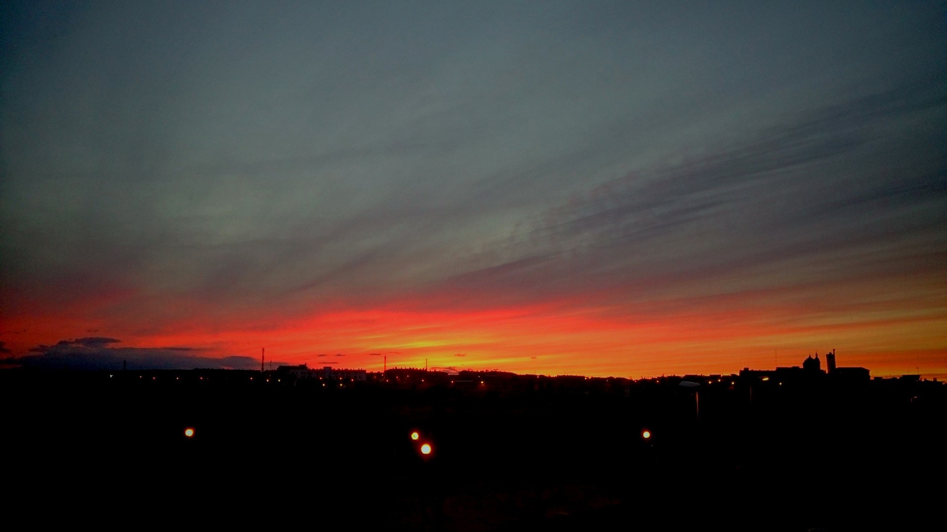 Sunset over a silhouetted cityscape with glowing lights HD Wallpaper