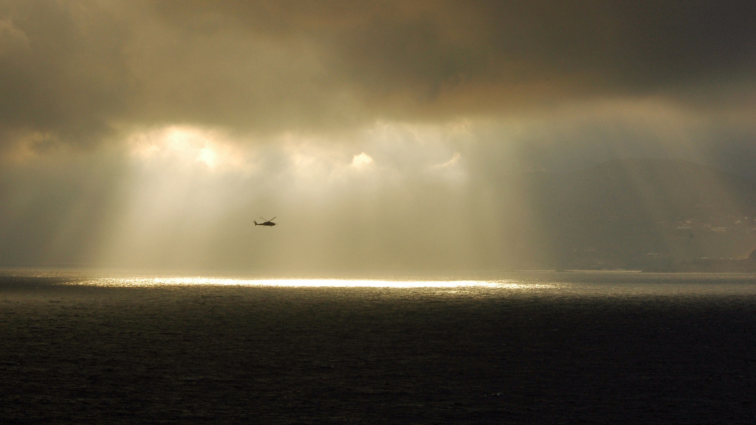 Helicopter flying over the sea during a sunbeam through clouds HD Wallpaper