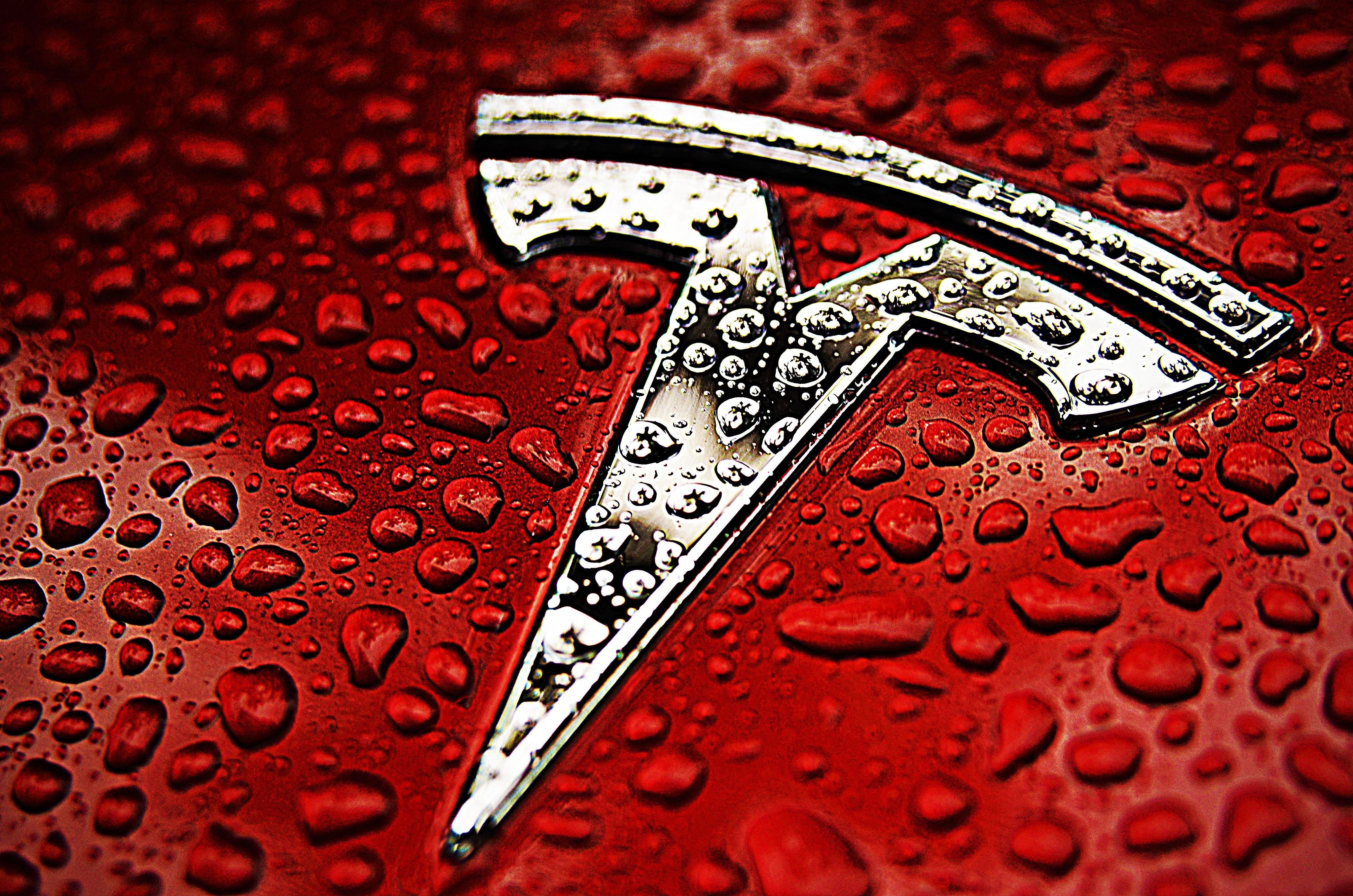 Tesla logo on a red surface with water droplets HD Wallpaper